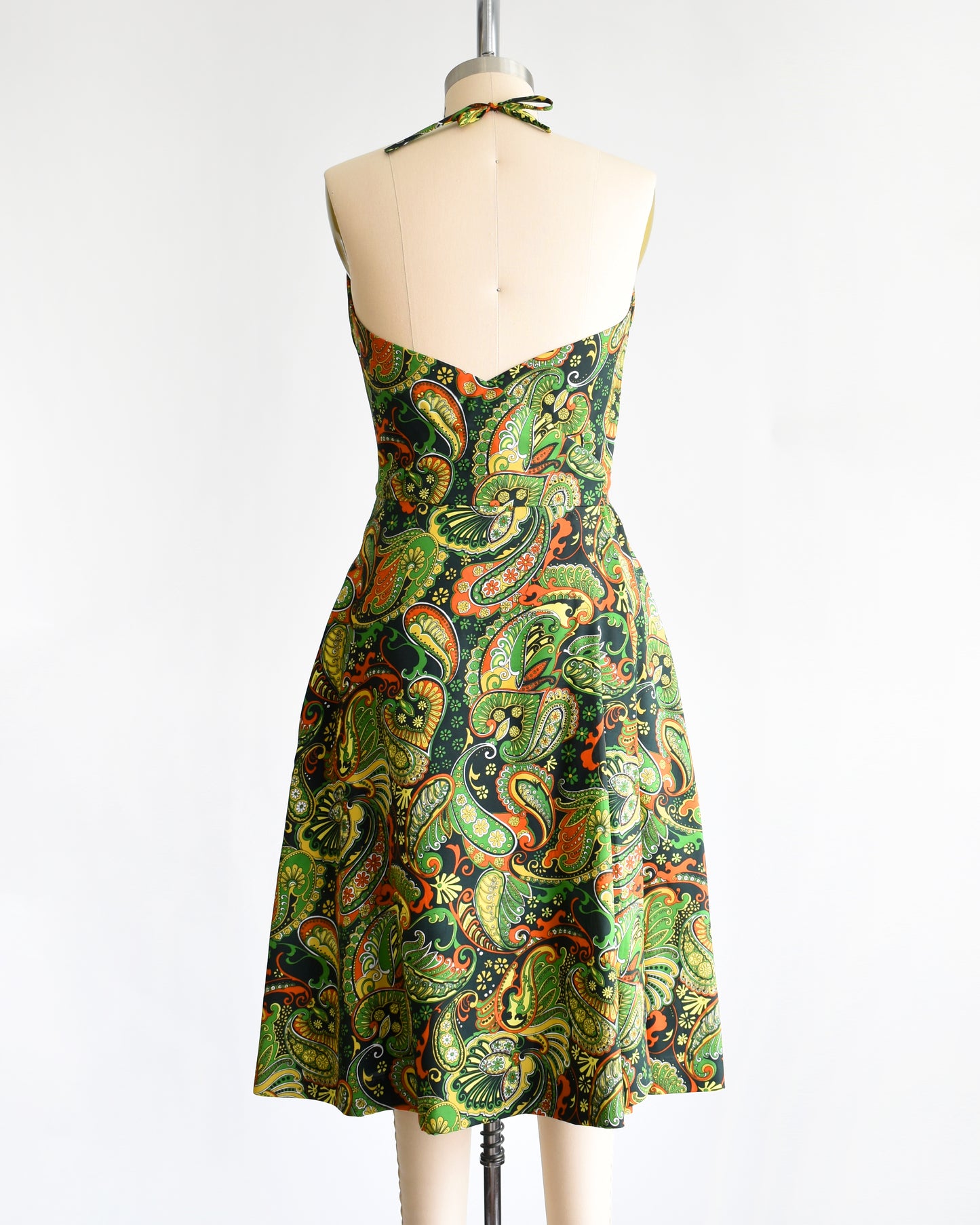 back view of a vintage 1970s psychedelic paisley dress on a mannequin against a white background