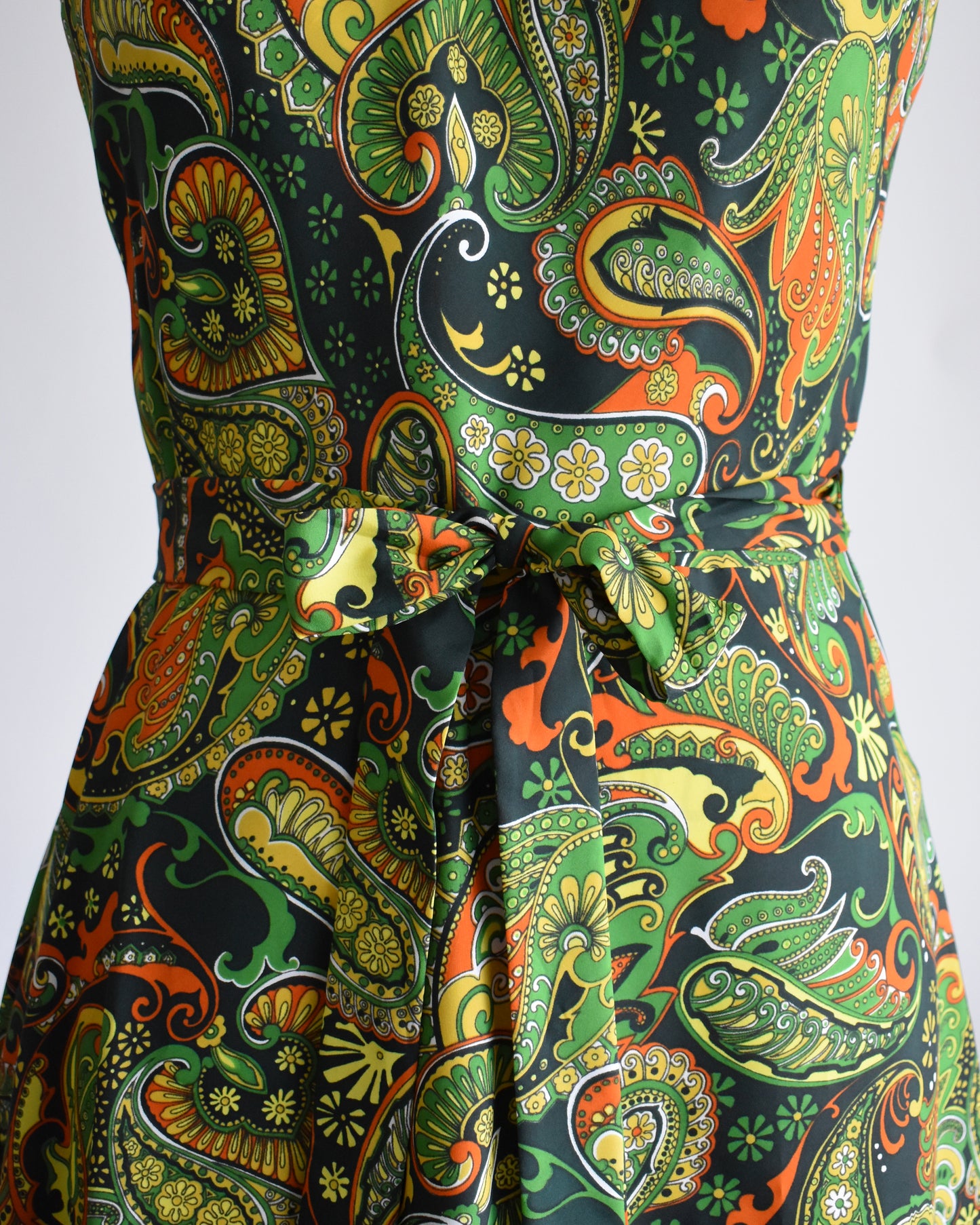 close up of the tied waist of a vintage 1970s psychedelic paisley dress on a mannequin against a white background