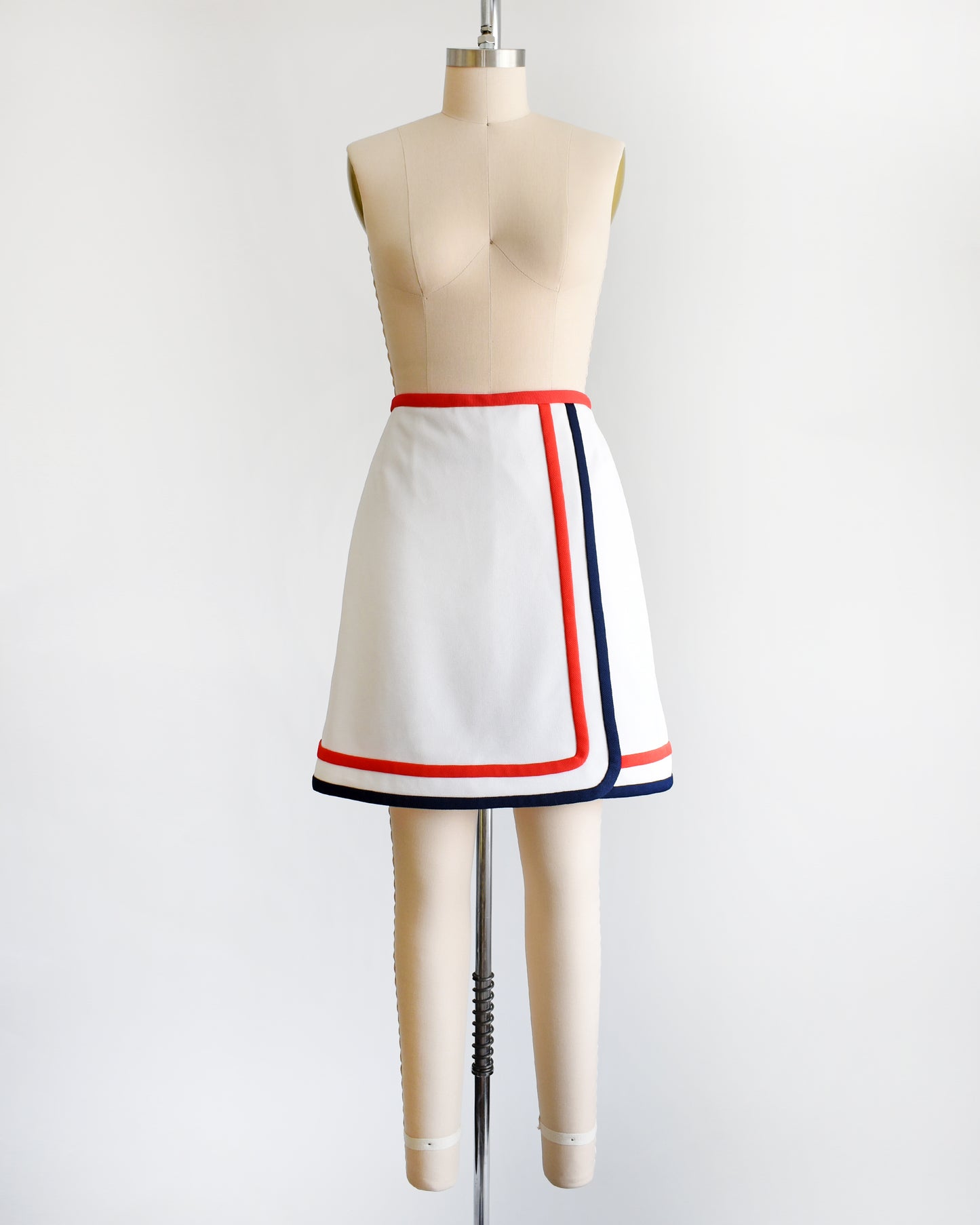 A vintage 1970s white skort with red and navy trim on a dress form against a white background