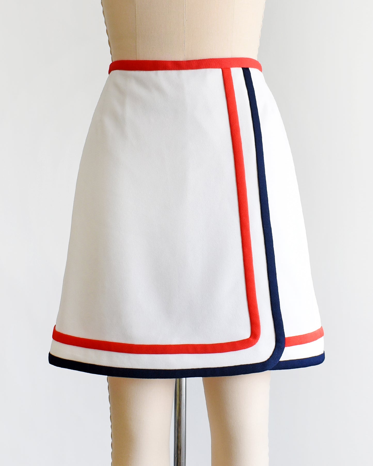 A vintage 1970s white skort with red and navy trim on a dress form against a white background