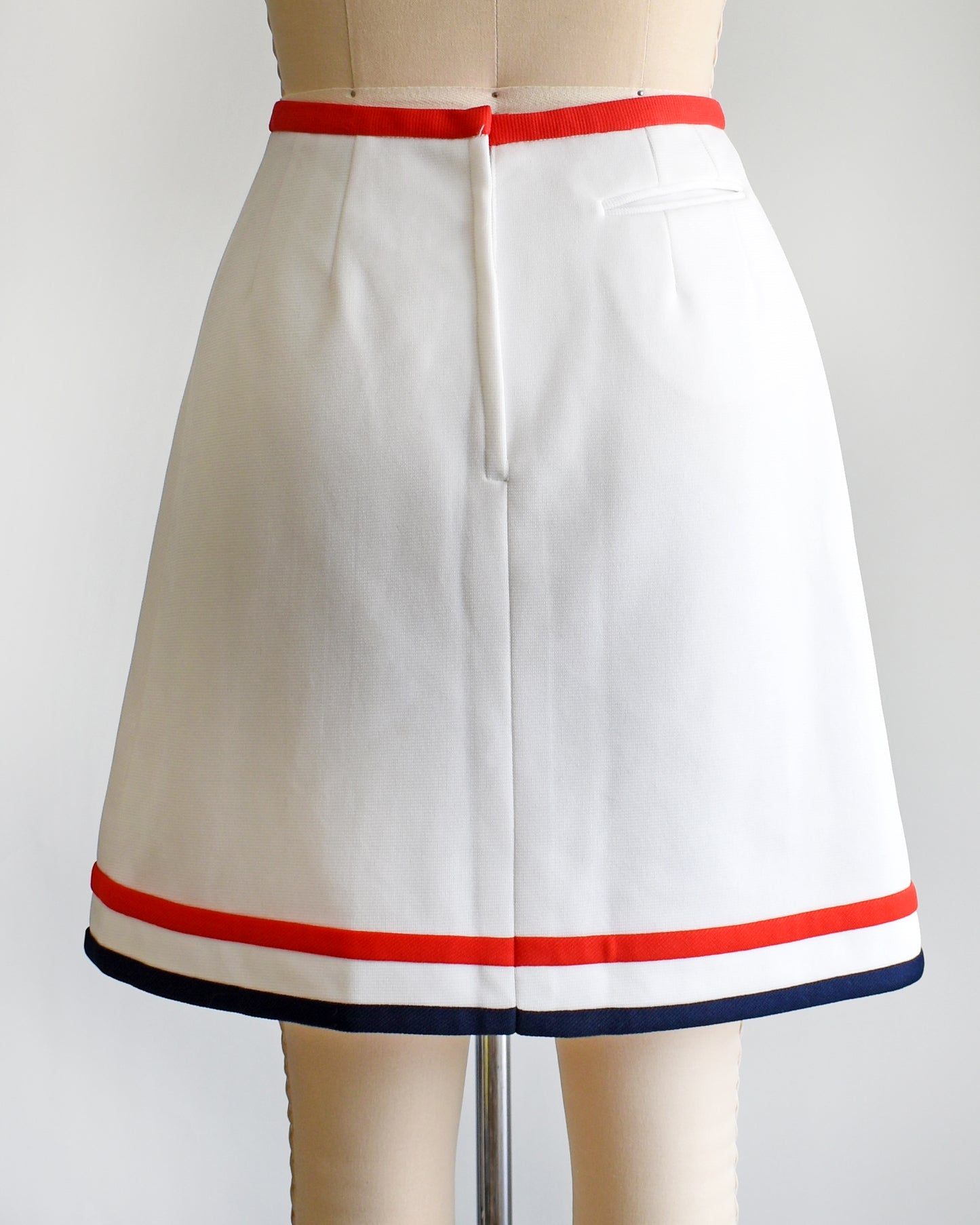 back view of a vintage 1970s white skort with red and navy trim on a dress form against a white background