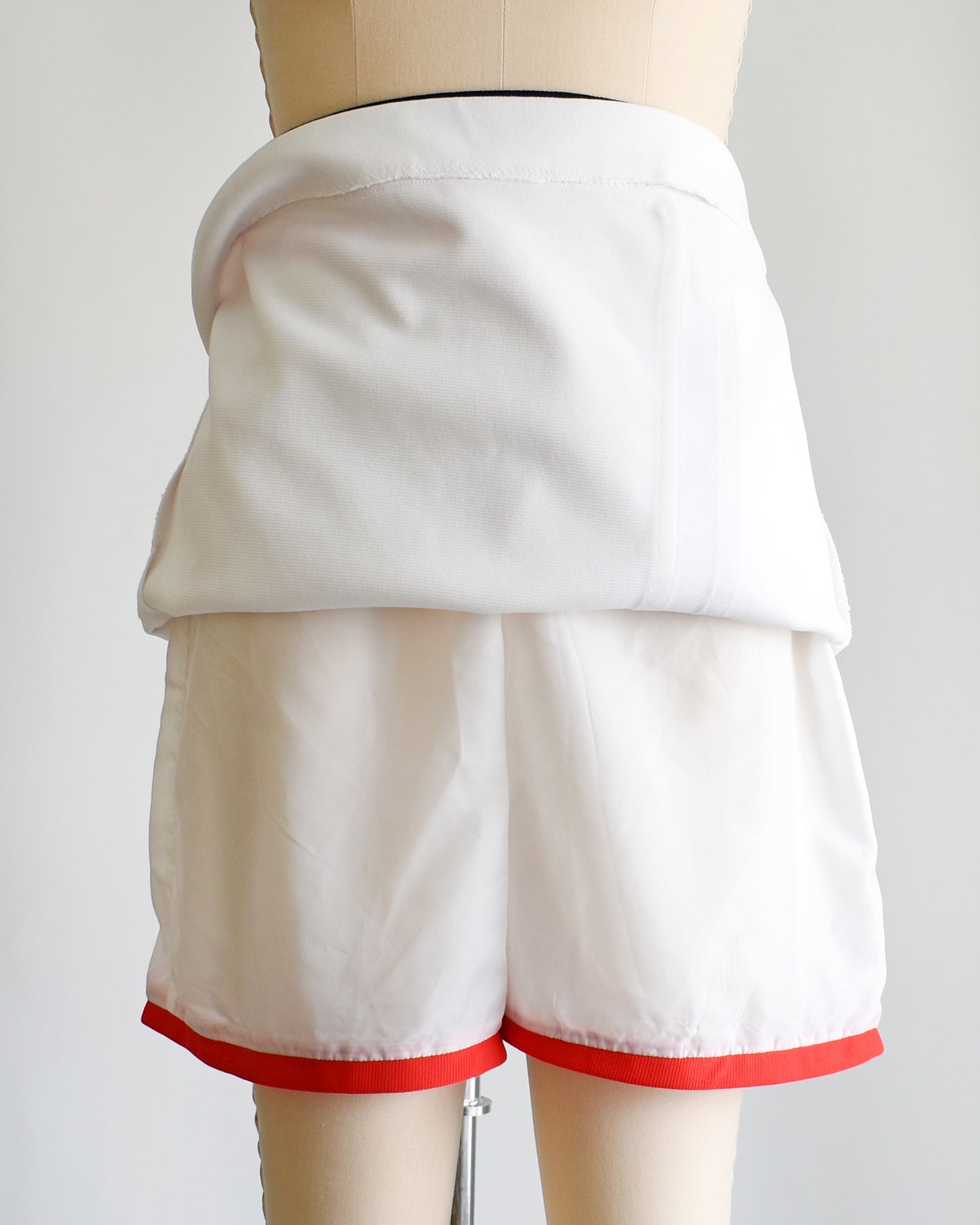 a vintage 1970s white skort with red and navy trim on a dress form against a white background. the skirt is lifted up showing the shorts underneath