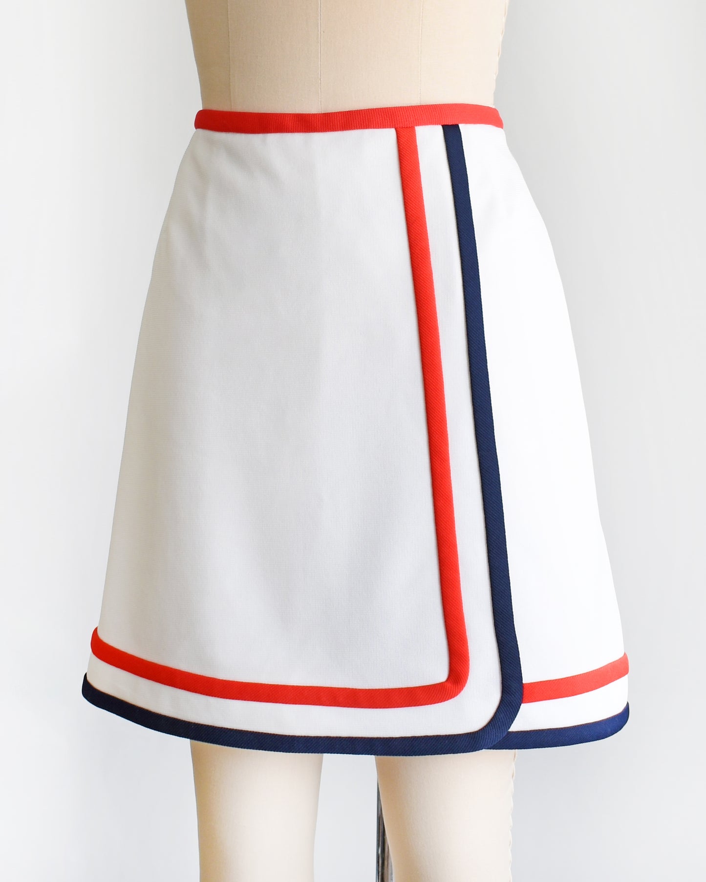 side front view of a vintage 1970s white skort with red and navy trim on a dress form against a white background