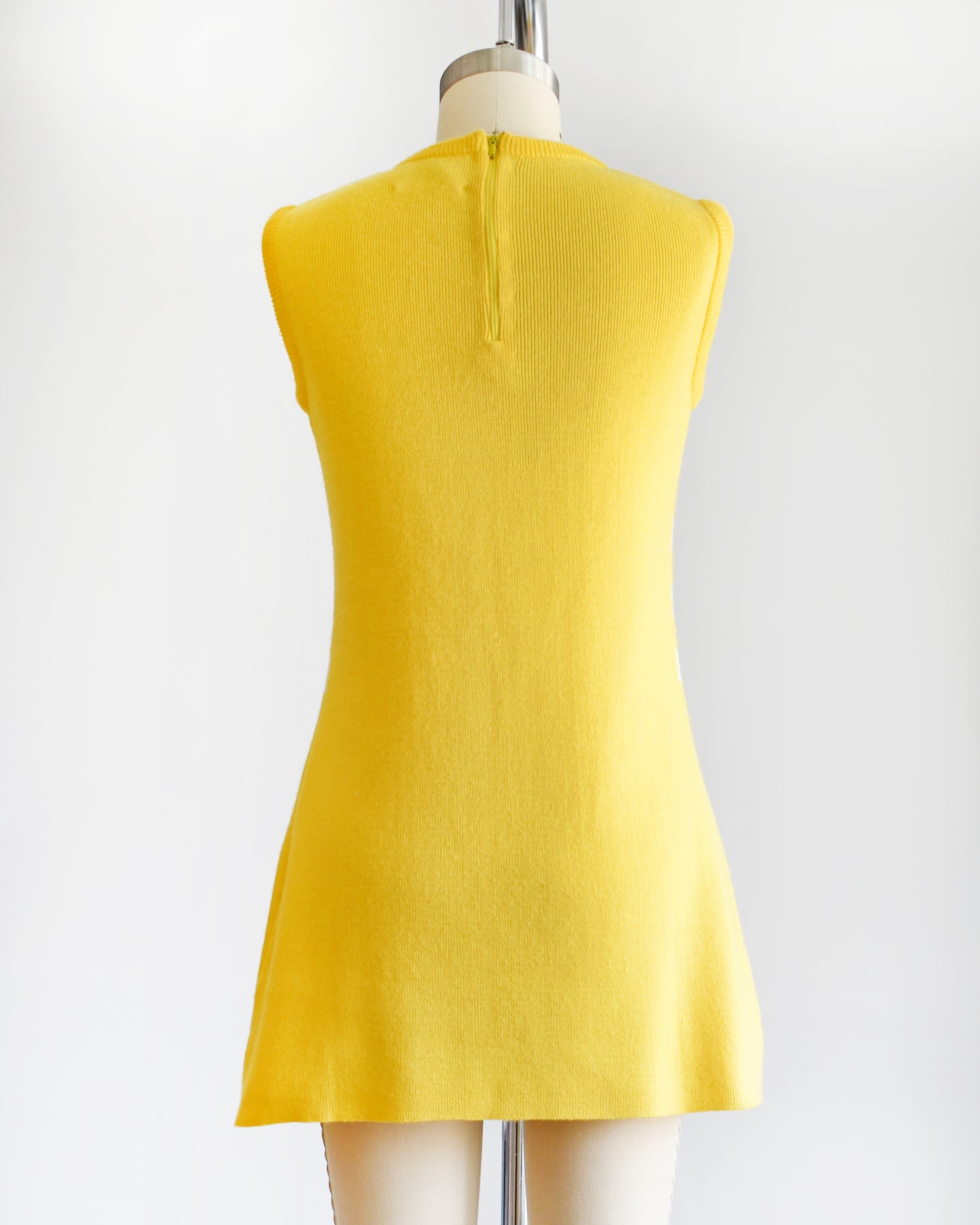 back view of a vintage 1970s yellow dress with floral design on a mannequin against a white background