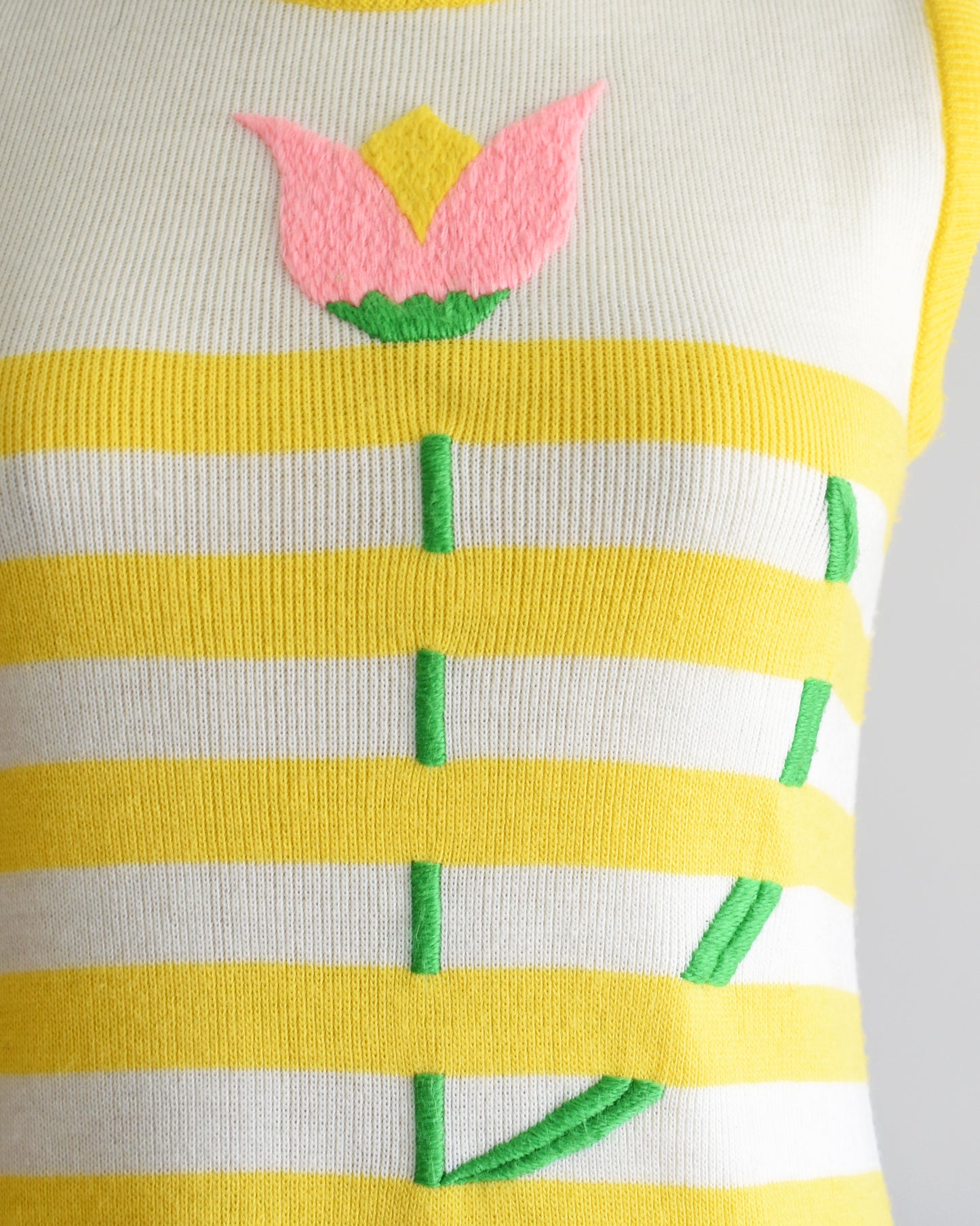 close up of the embroidered flower on a vintage 1970s yellow dress with floral design on a mannequin against a white background