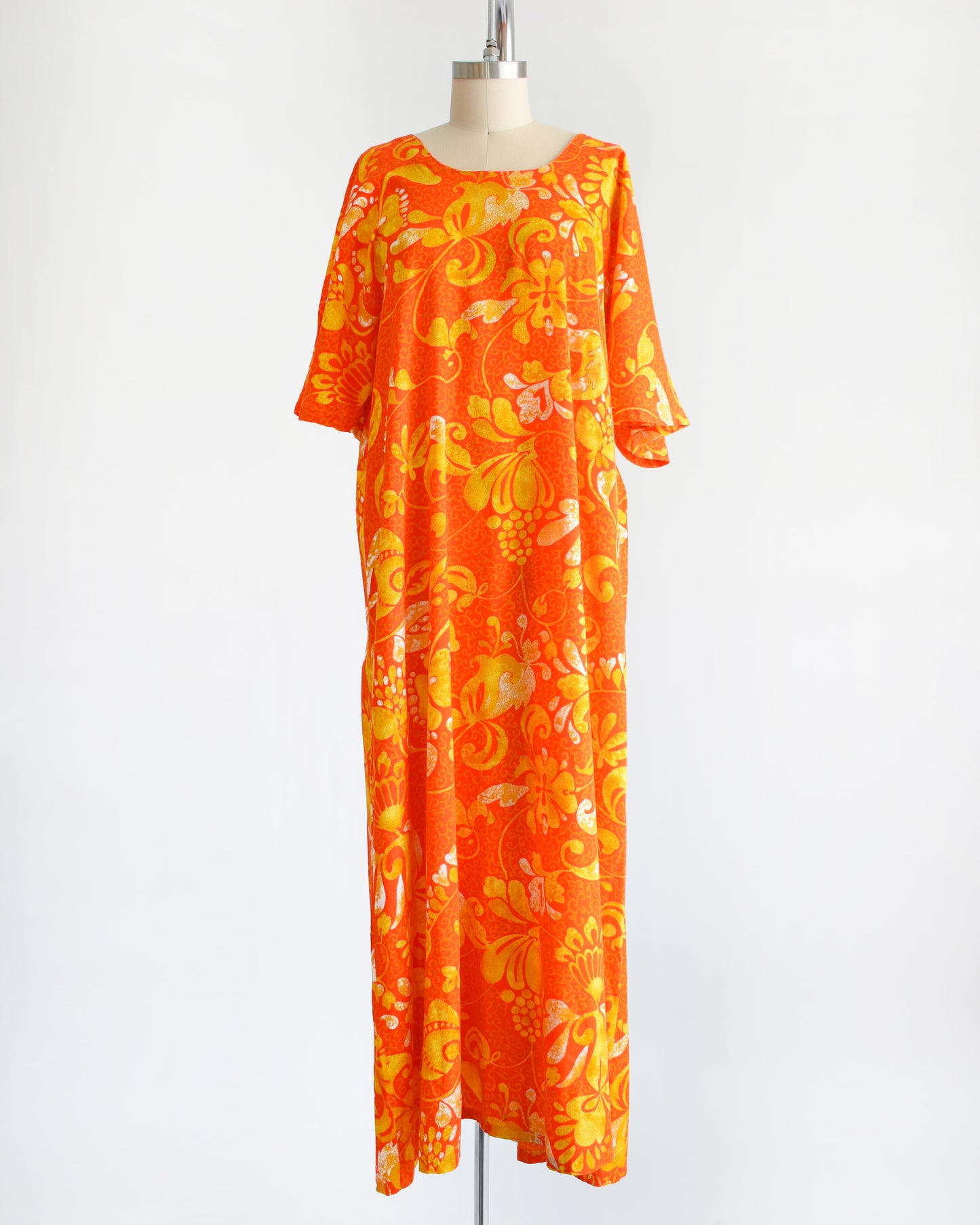 A vintage 1970s orange floral maxi caftan dress on a mannequin against a white background