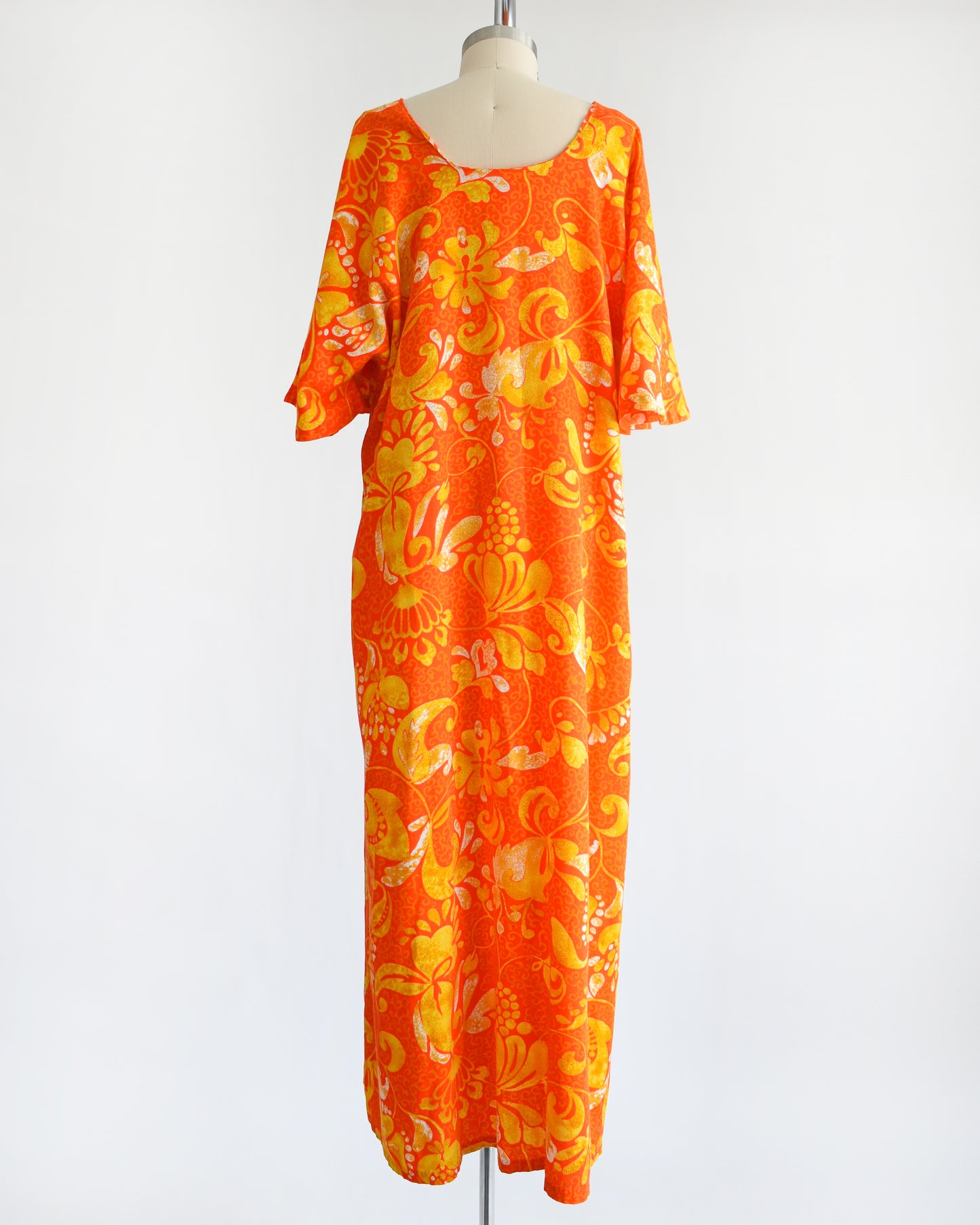 back view of a vintage 1970s orange floral maxi caftan dress on a mannequin against a white background