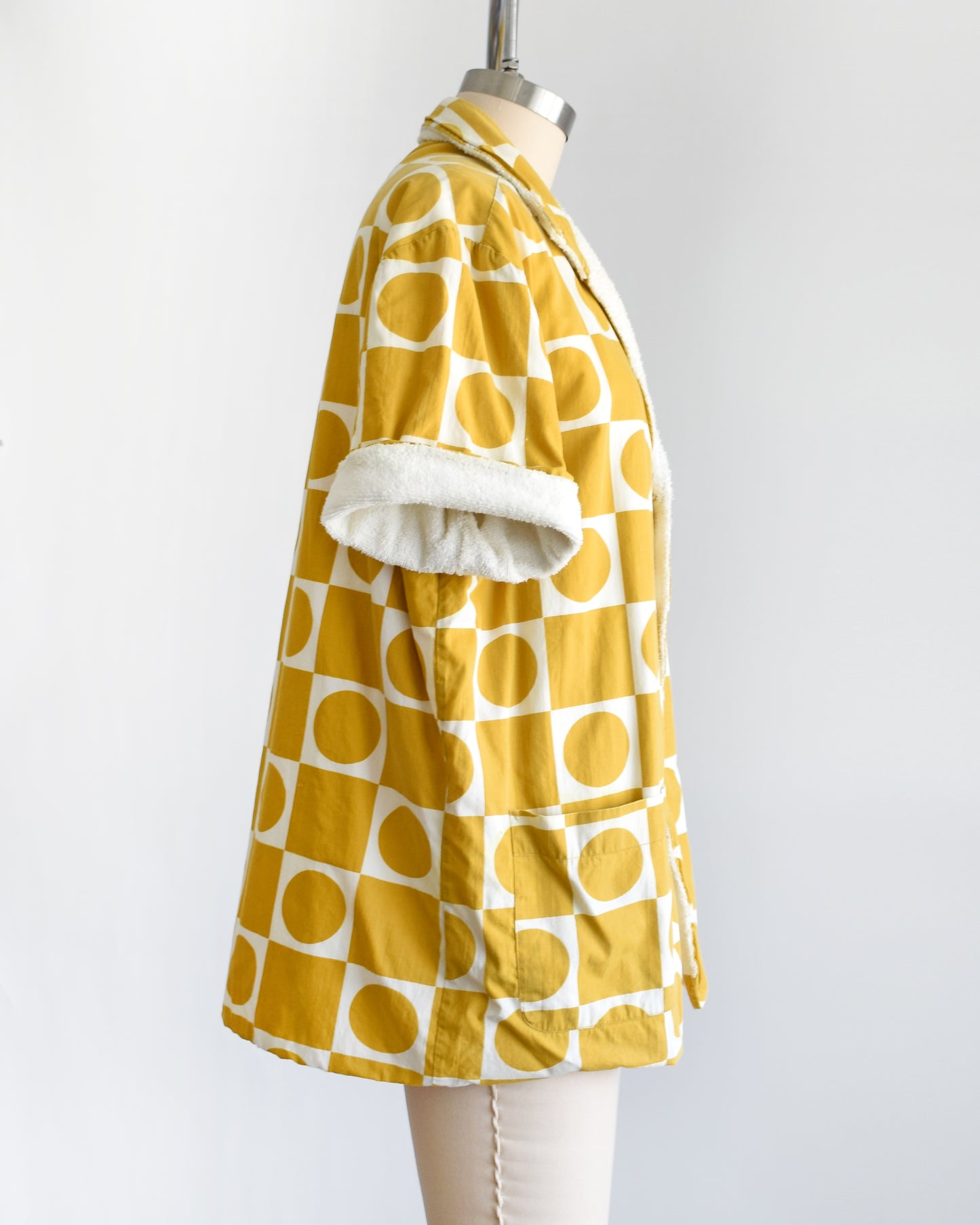 side view of a vintage 1960s mustard yellow patterned cabana shirt with white terry clothing lining on a mannequin against a white background
