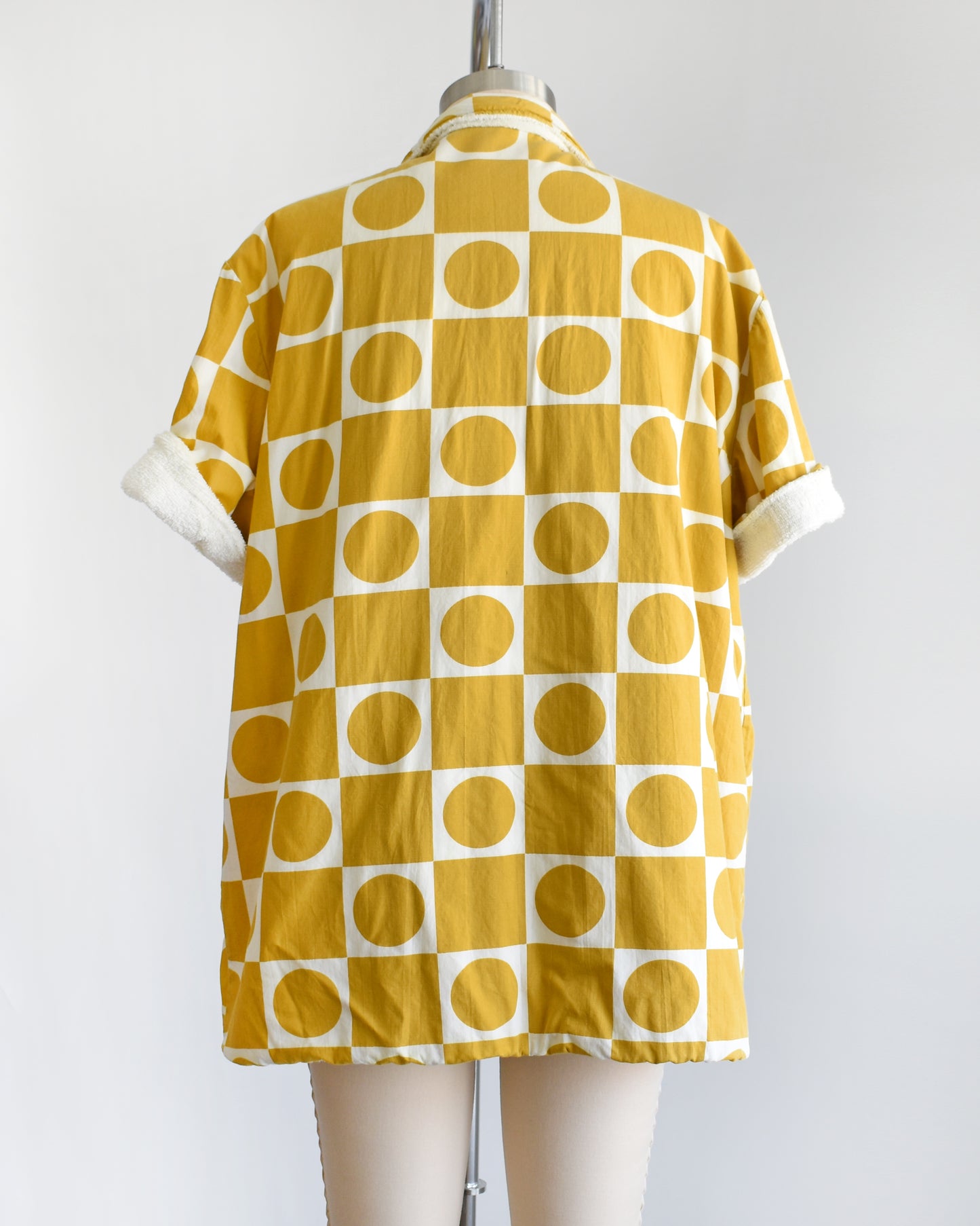 back view of a vintage 1960s mustard yellow patterned cabana shirt with white terry clothing lining on a mannequin against a white background