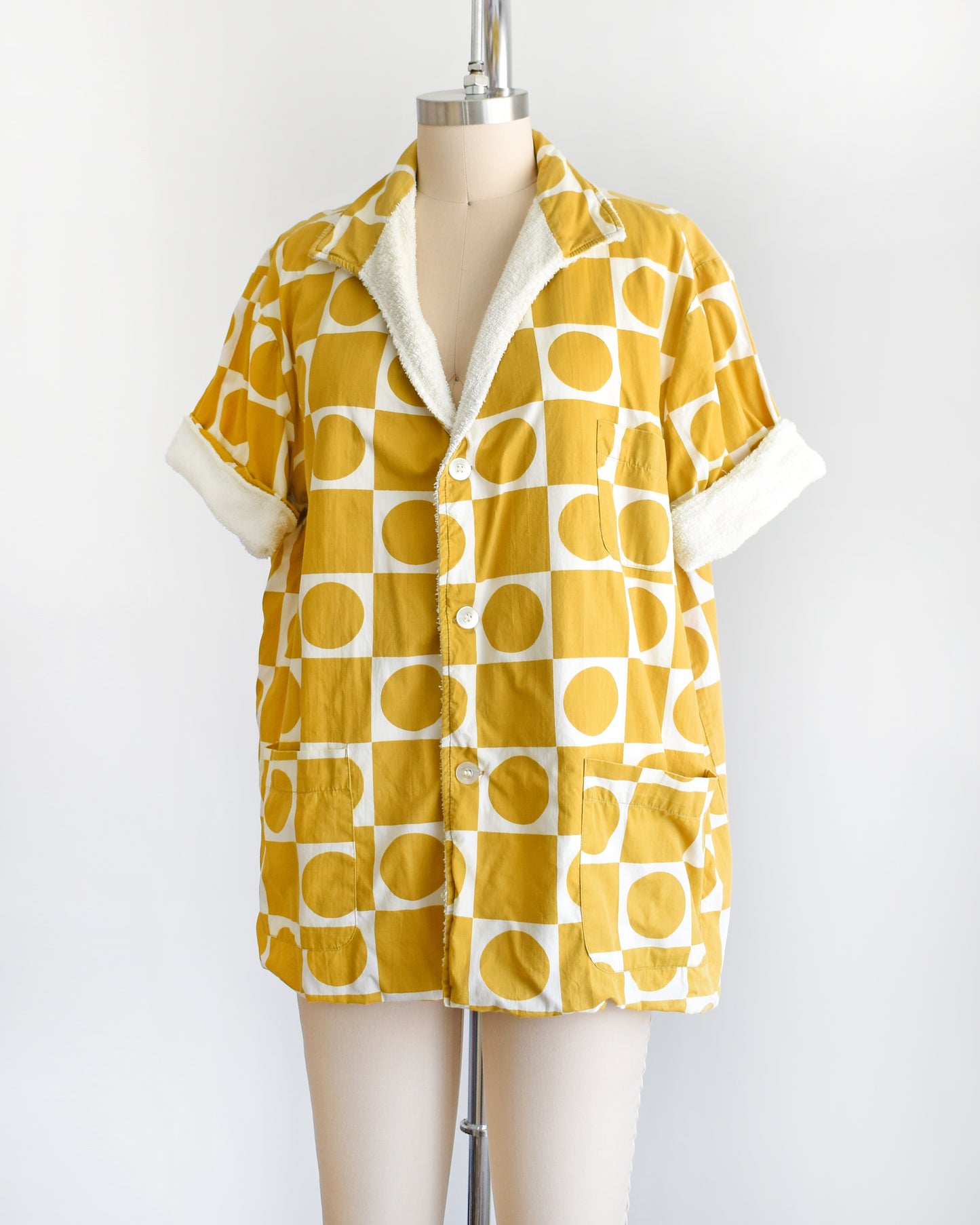 side front view of a vintage 1960s mustard yellow patterned cabana shirt with white terry clothing lining on a mannequin against a white background