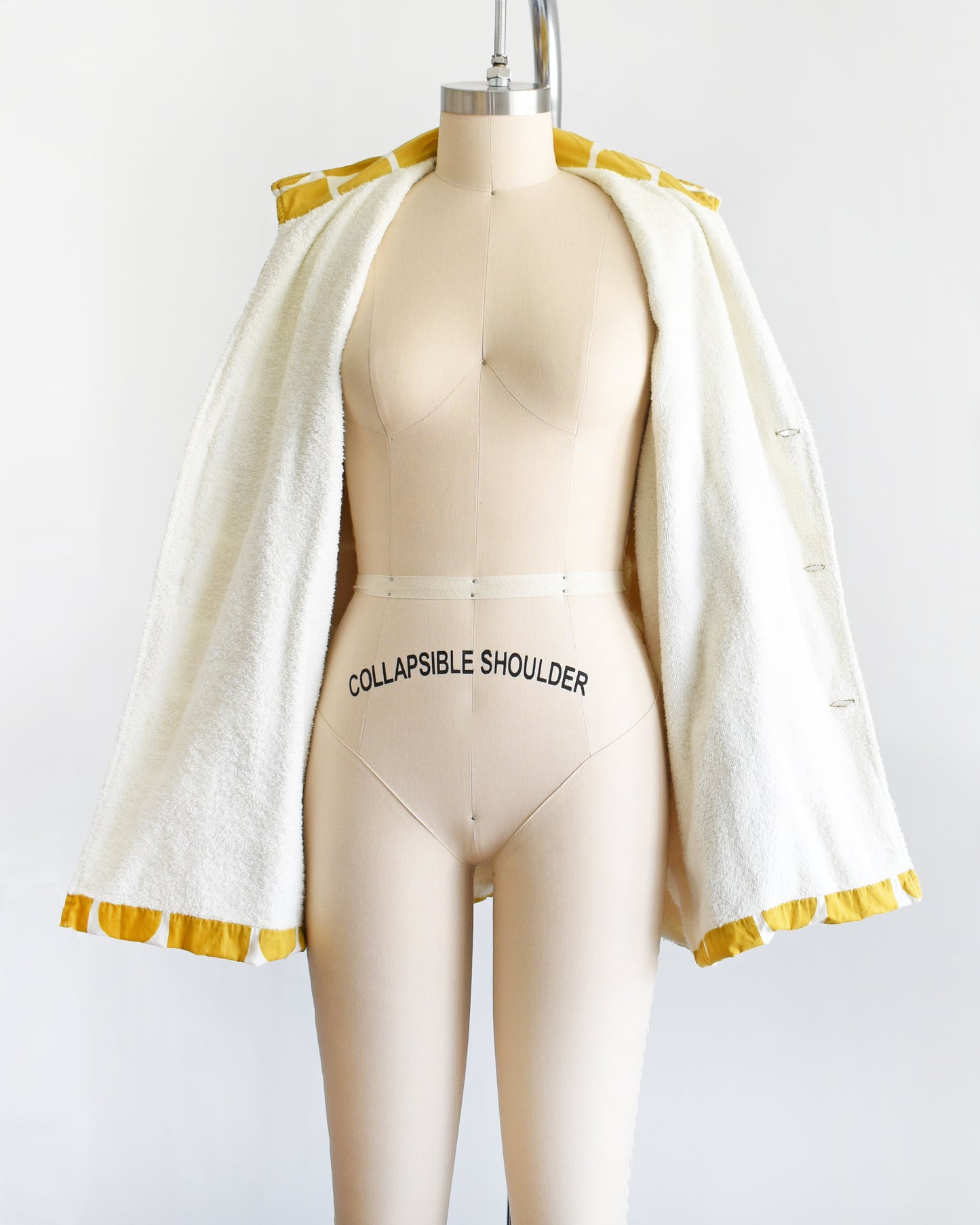 a vintage 1960s mustard yellow patterned cabana shirt with white terry clothing lining on a mannequin against a white background. the shirt is open showing the white terry cloth lining.