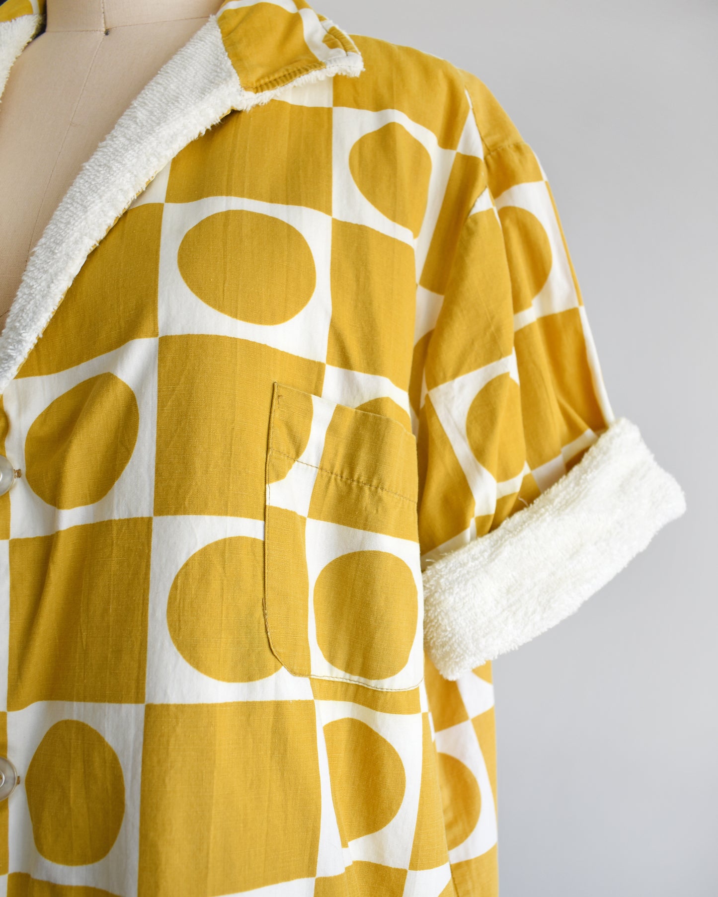 close up of the patch pocket on a vintage 1960s mustard yellow patterned cabana shirt with white terry clothing lining on a mannequin against a white background