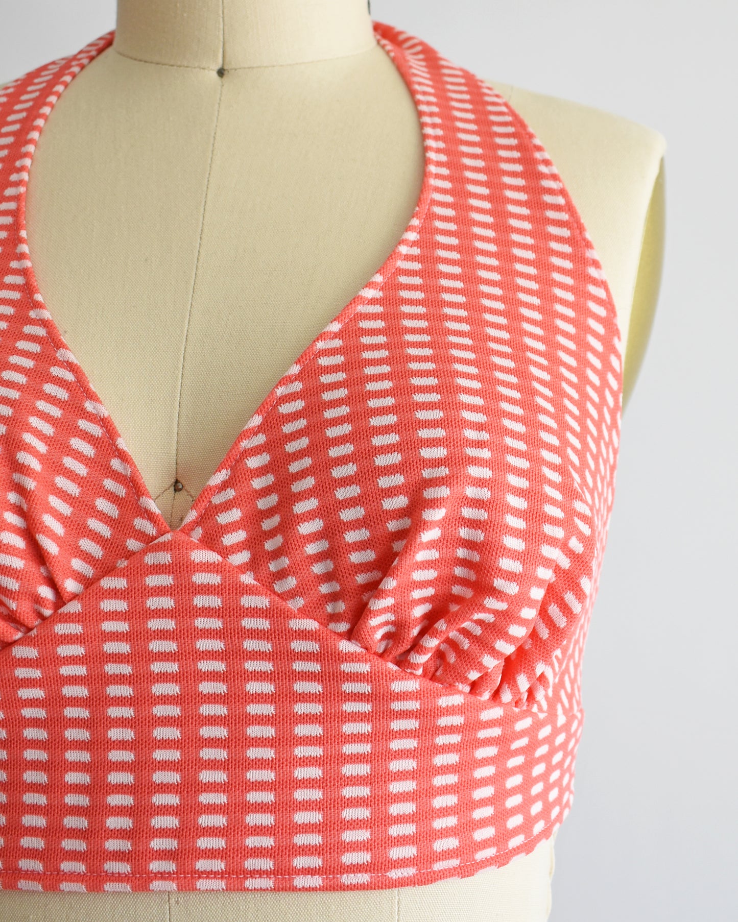 close up of the halter top which is coral pink and has a white rectangle print