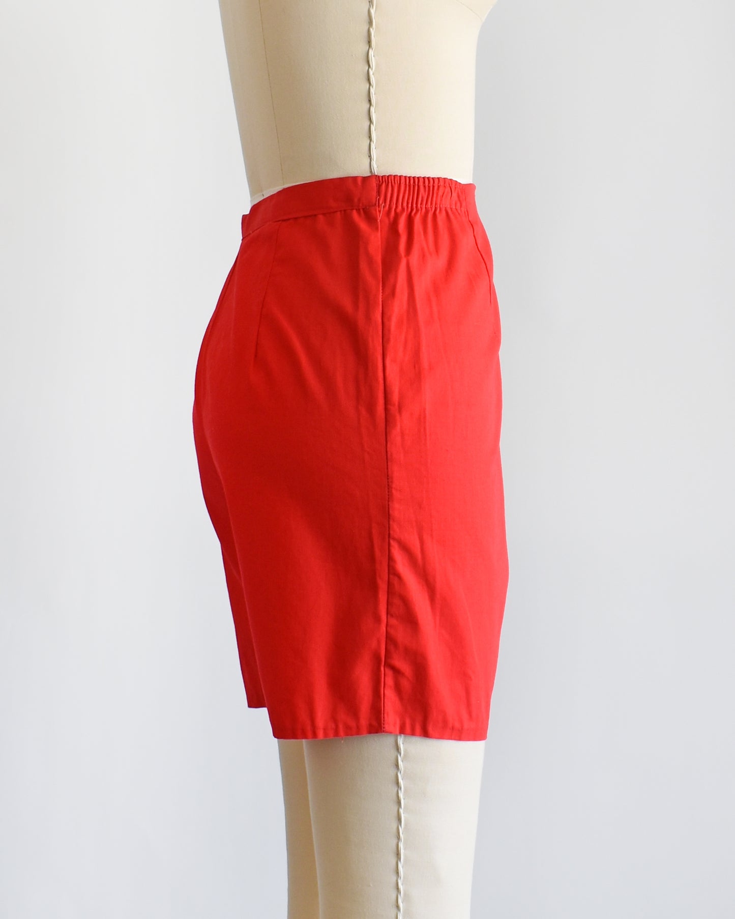 side view of a pair of vintage 1960s red shorts on a mannequin against a white background