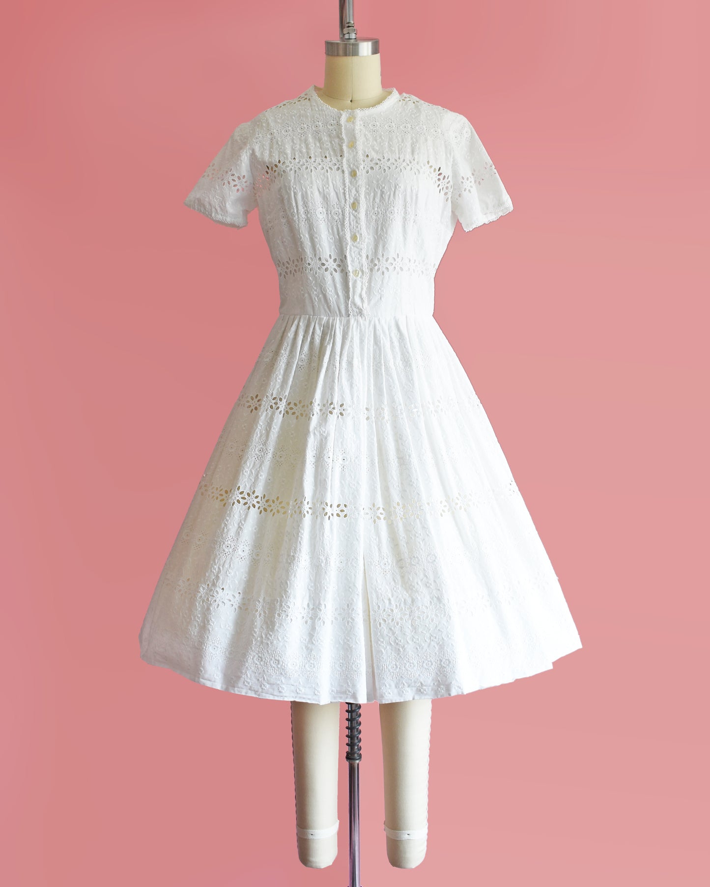 a vintage 1960s L’Aiglon eyelet white dress on a mannequin against a pink background