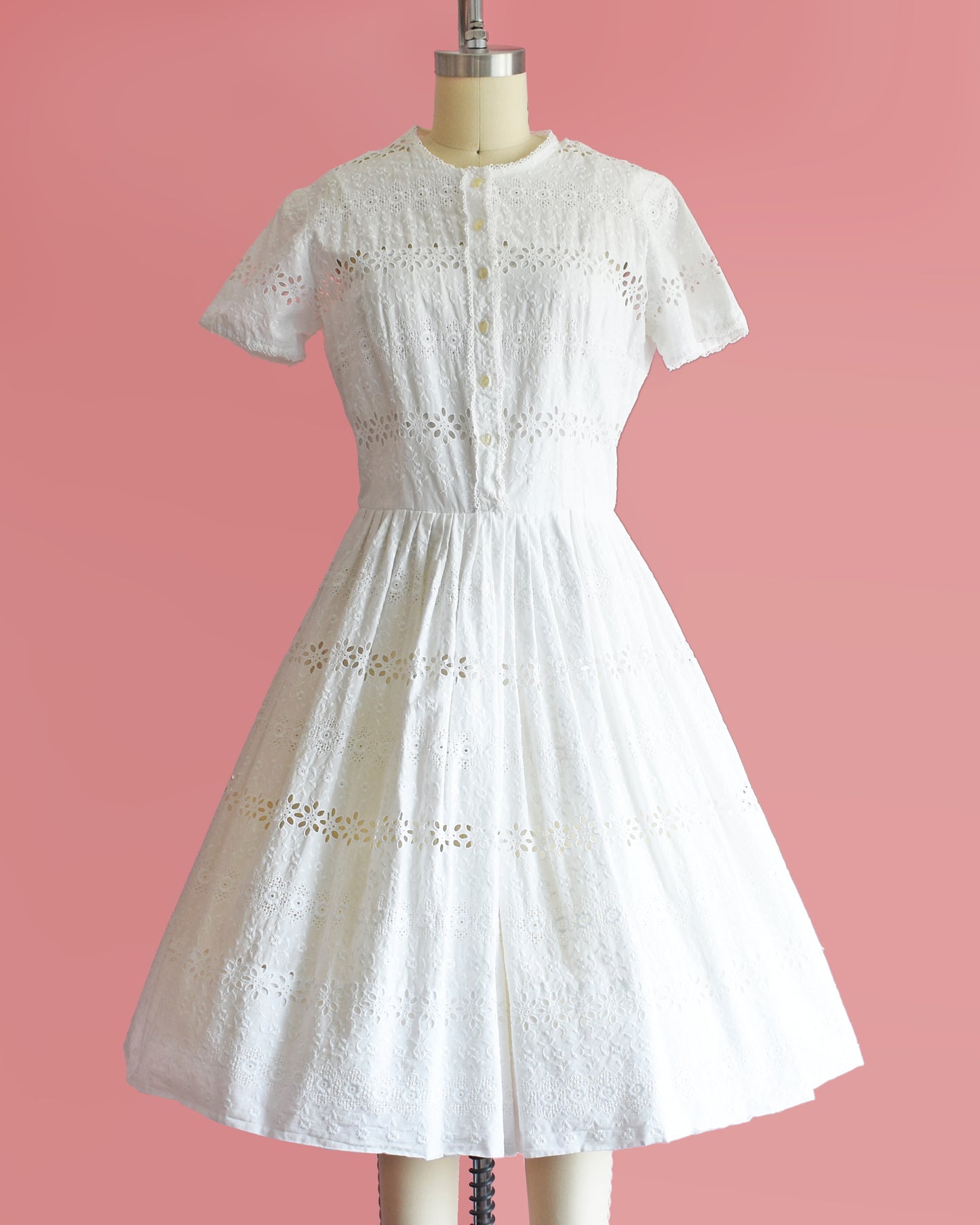 a vintage 1960s L’Aiglon eyelet white dress on a mannequin against a pink background