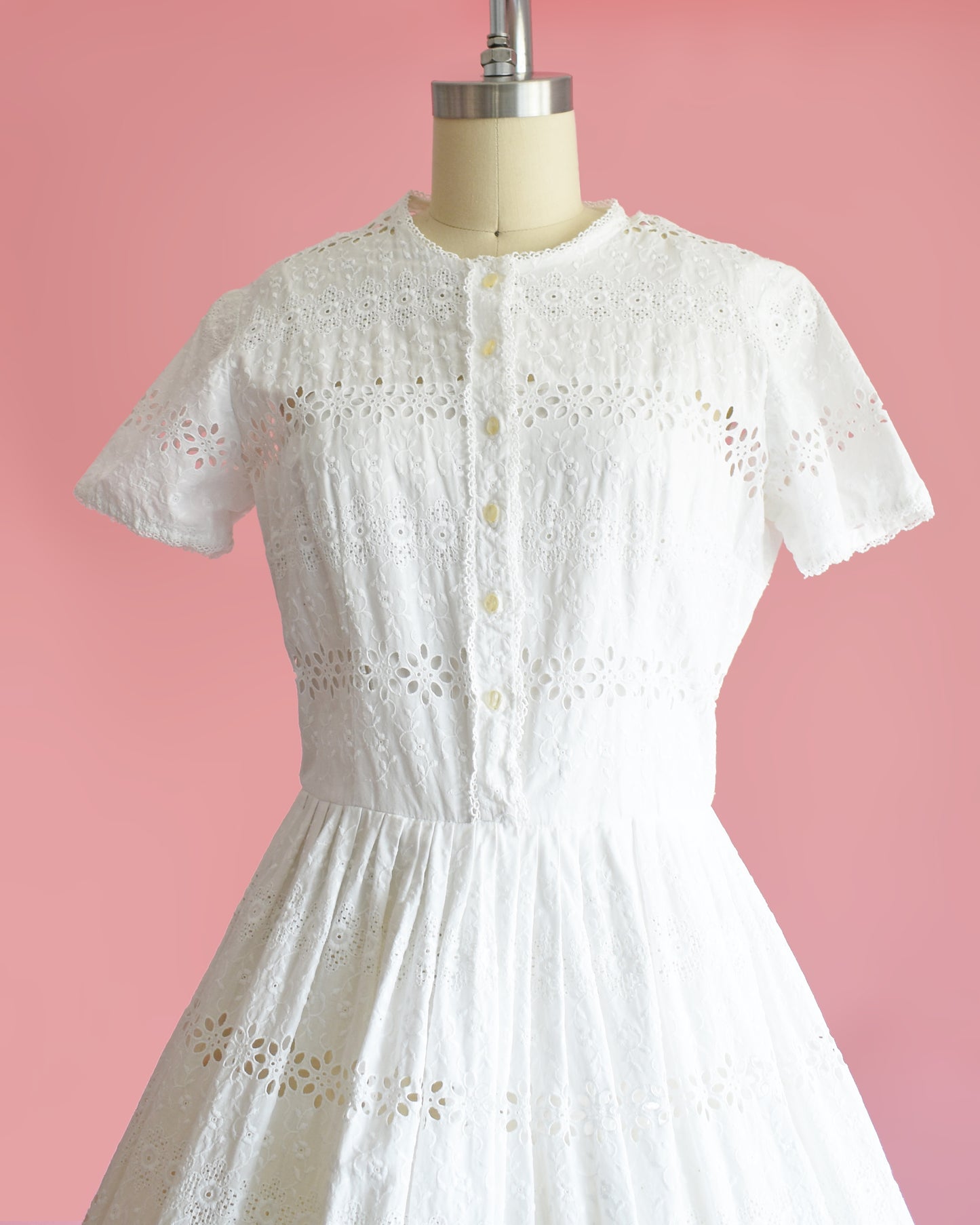 side front view of a vintage 1960s L’Aiglon eyelet white dress on a mannequin against a pink background