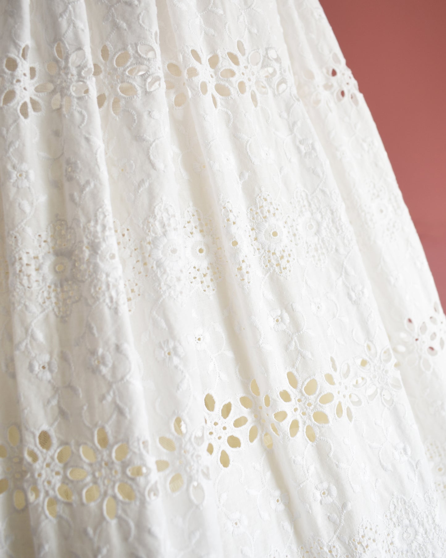 Close-up of white eyelet lace fabric with floral cut-out patterns on a pink background