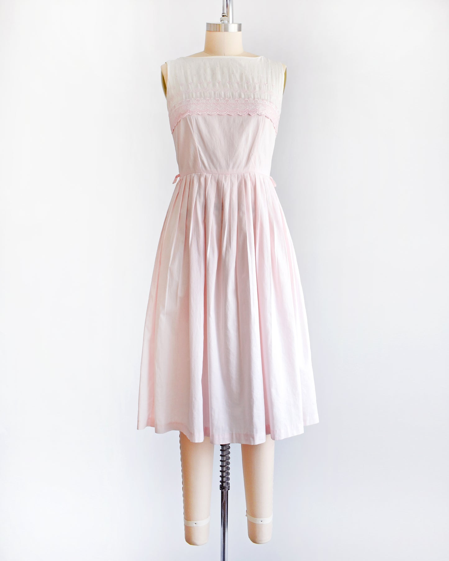 a vintage 1950s pink and white embroidered dress on a mannequin against a white background