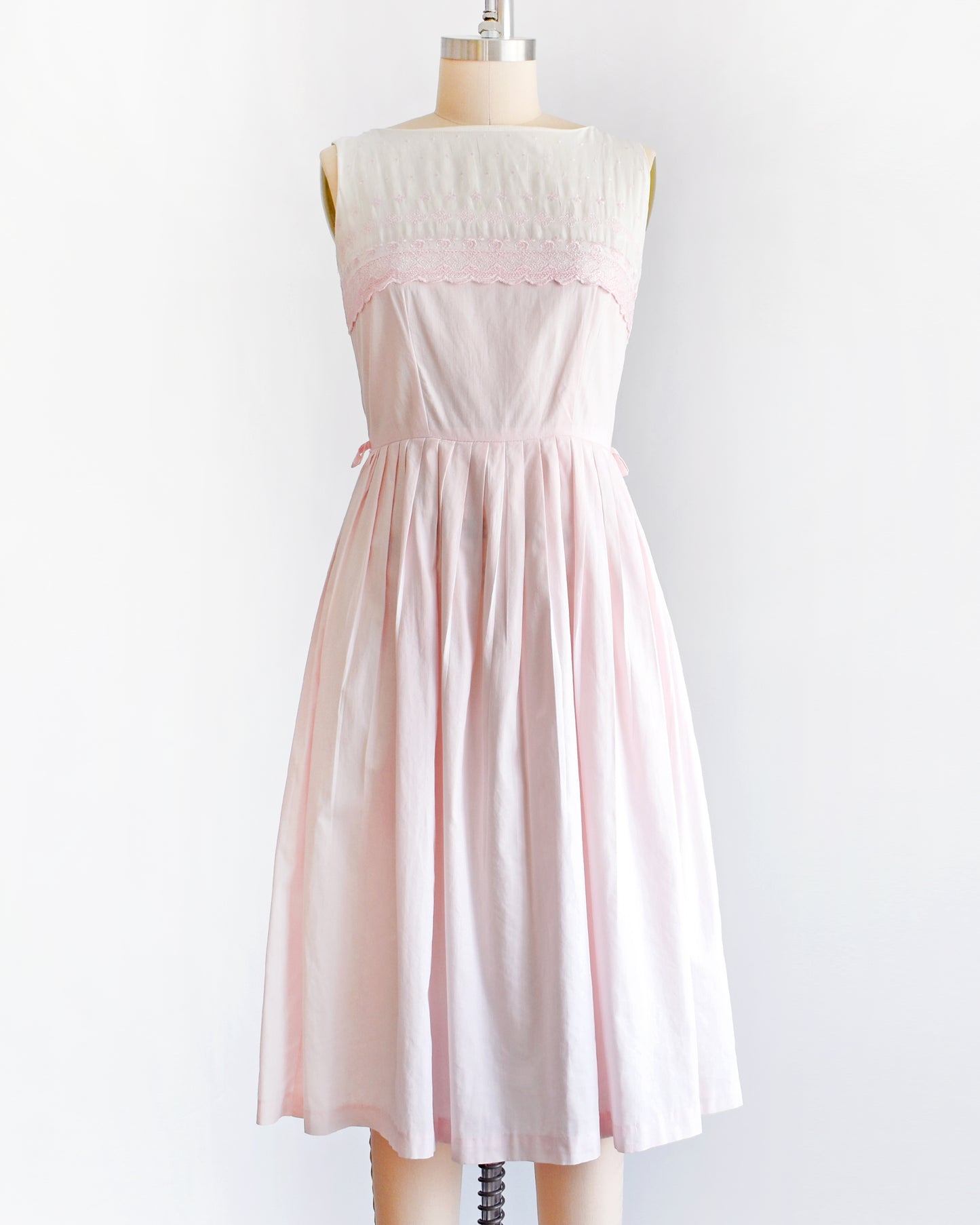 a vintage 1950s pink and white embroidered dress on a mannequin against a white background