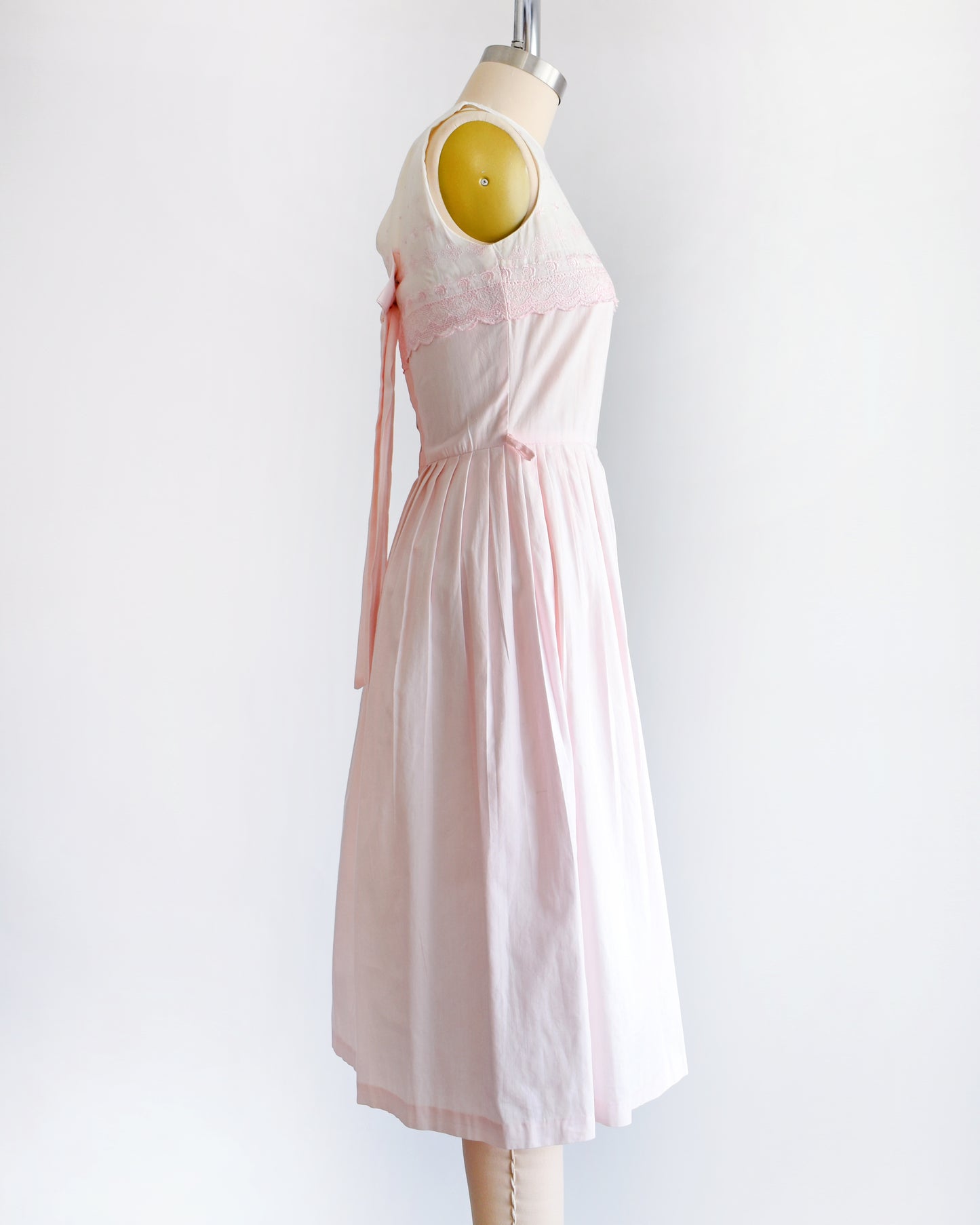 side view of a vintage 1950s pink and white embroidered dress on a mannequin against a white background