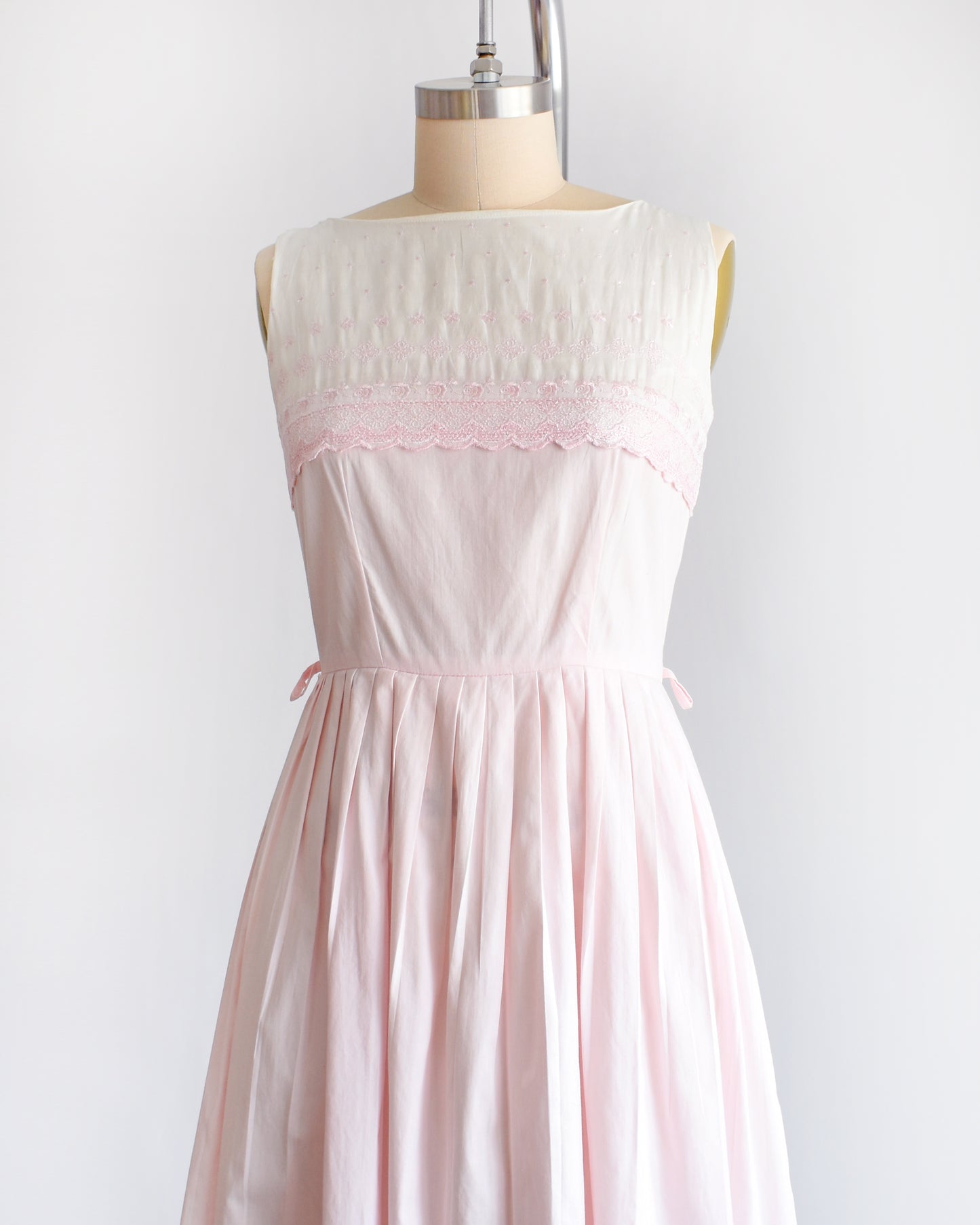 side front view of a vintage 1950s pink and white embroidered dress on a mannequin against a white background