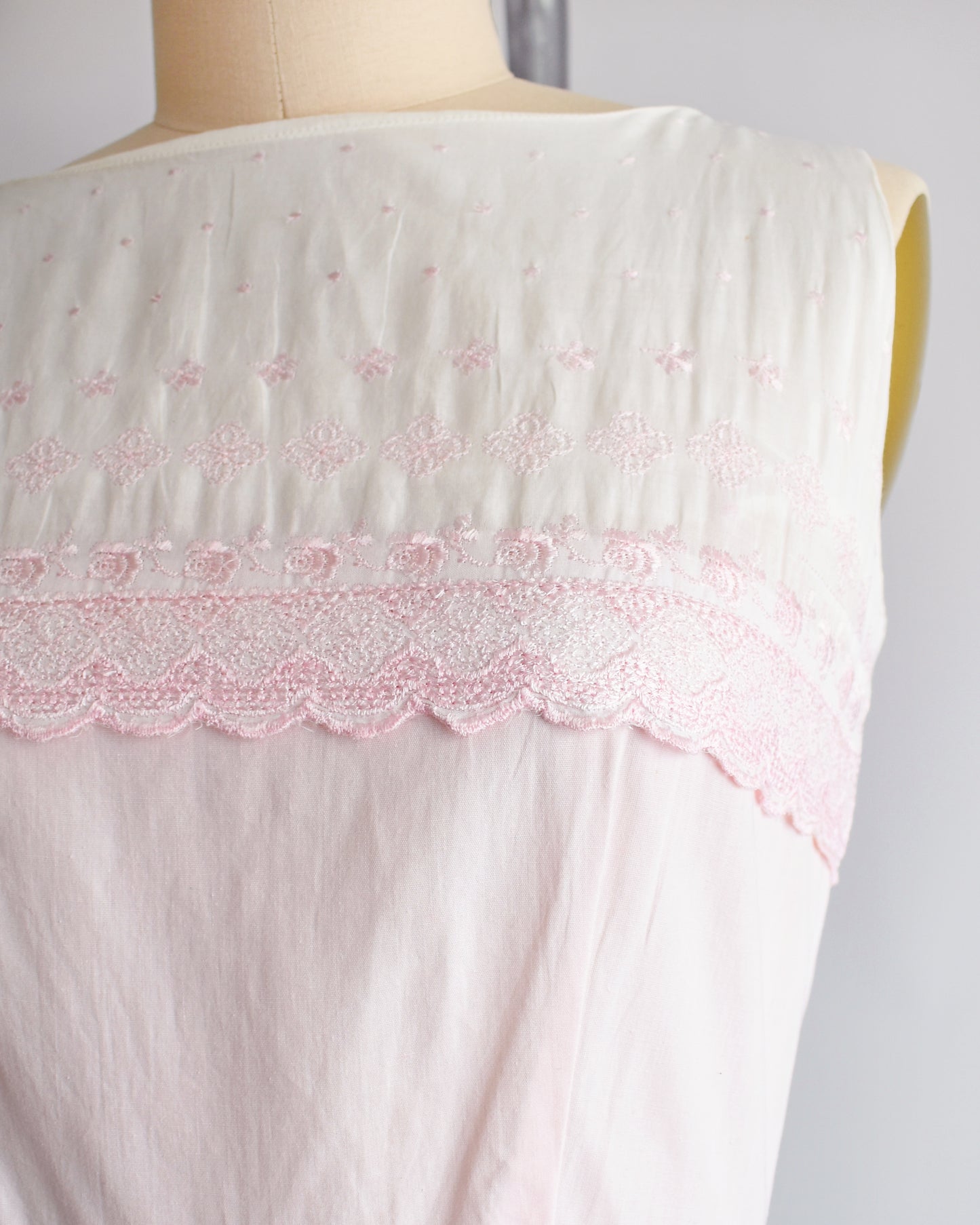 close up of the embroidered bodice on a vintage 1950s pink and white embroidered dress on a mannequin against a white background