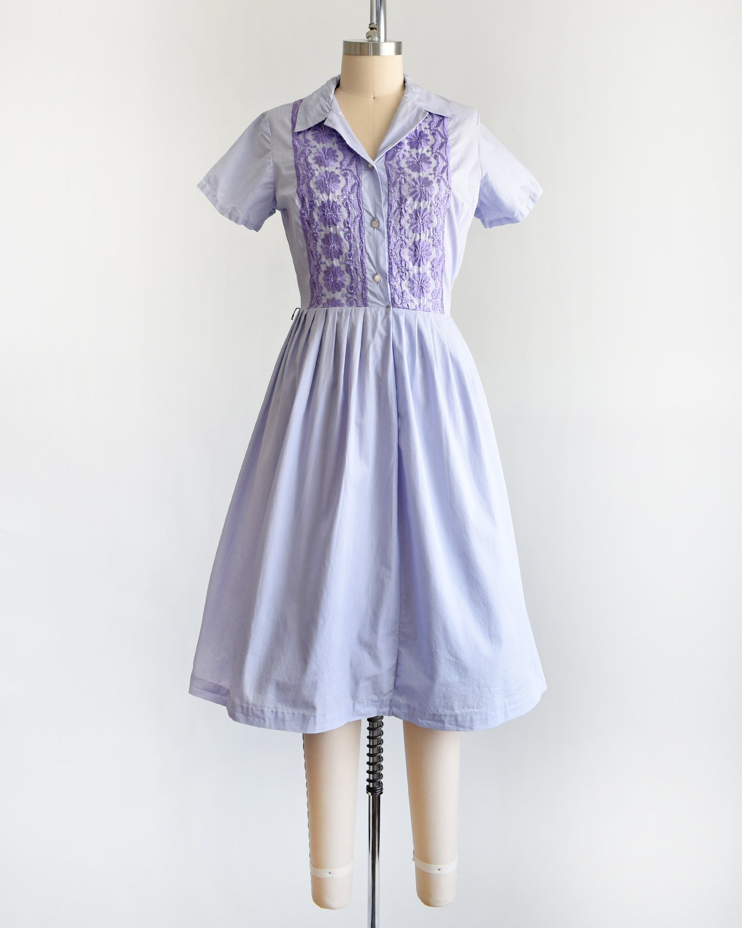 a vintage 1950s light purple dress with dark purple embroidery on a mannequin against a white background
