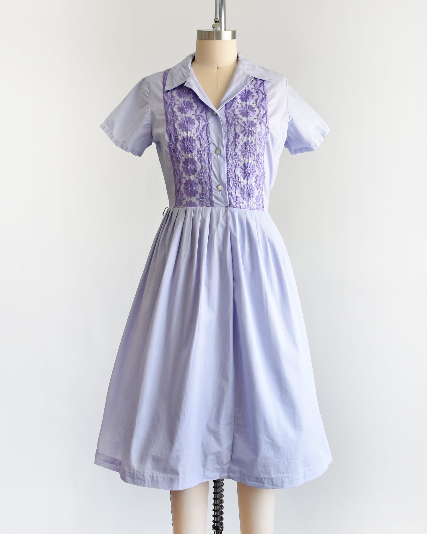 a vintage 1950s light purple dress with dark purple embroidery on a mannequin against a white background