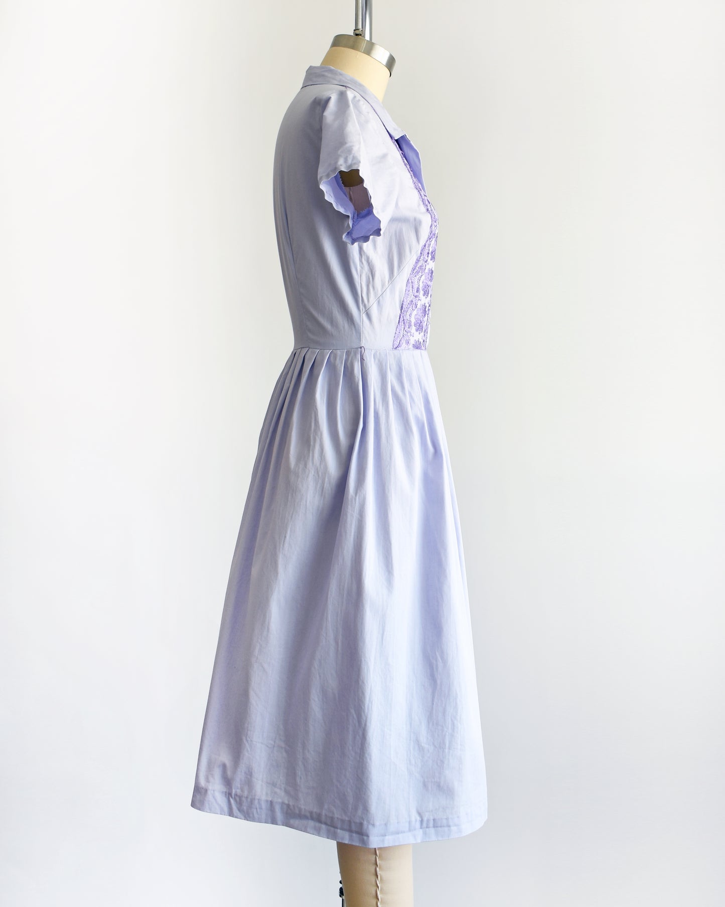 side view of a vintage 1950s light purple dress with dark purple embroidery on a mannequin against a white background