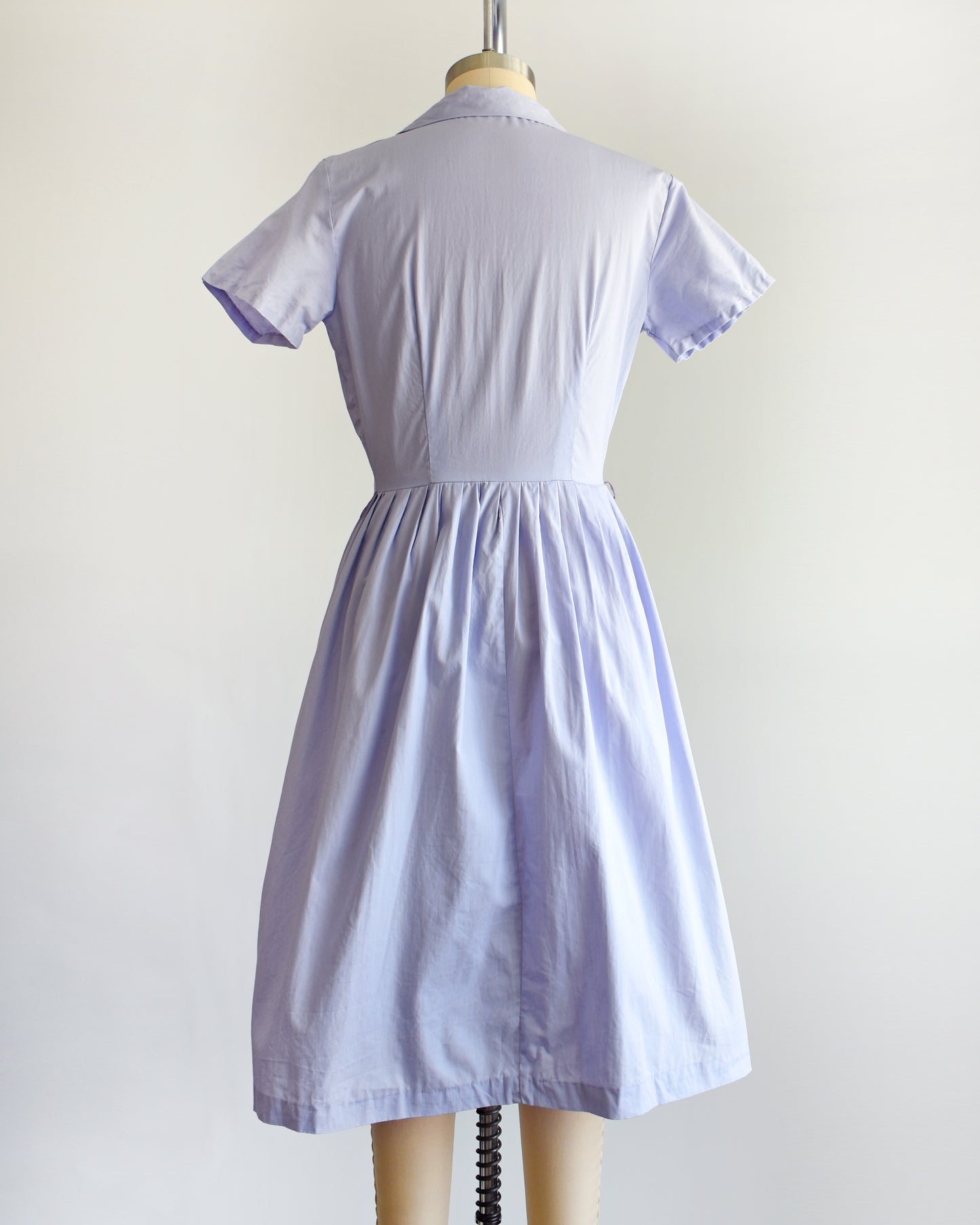 back view of a vintage 1950s light purple dress on a mannequin against a white background