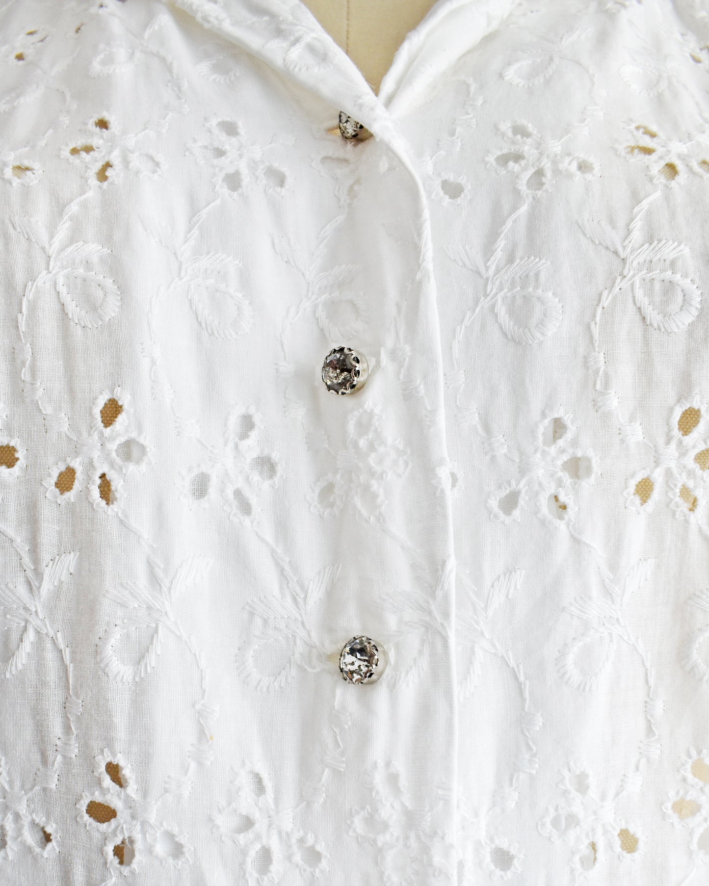 close up of the rhinestone buttons and eyelet detail on a vintage 1950s white eyelet dress