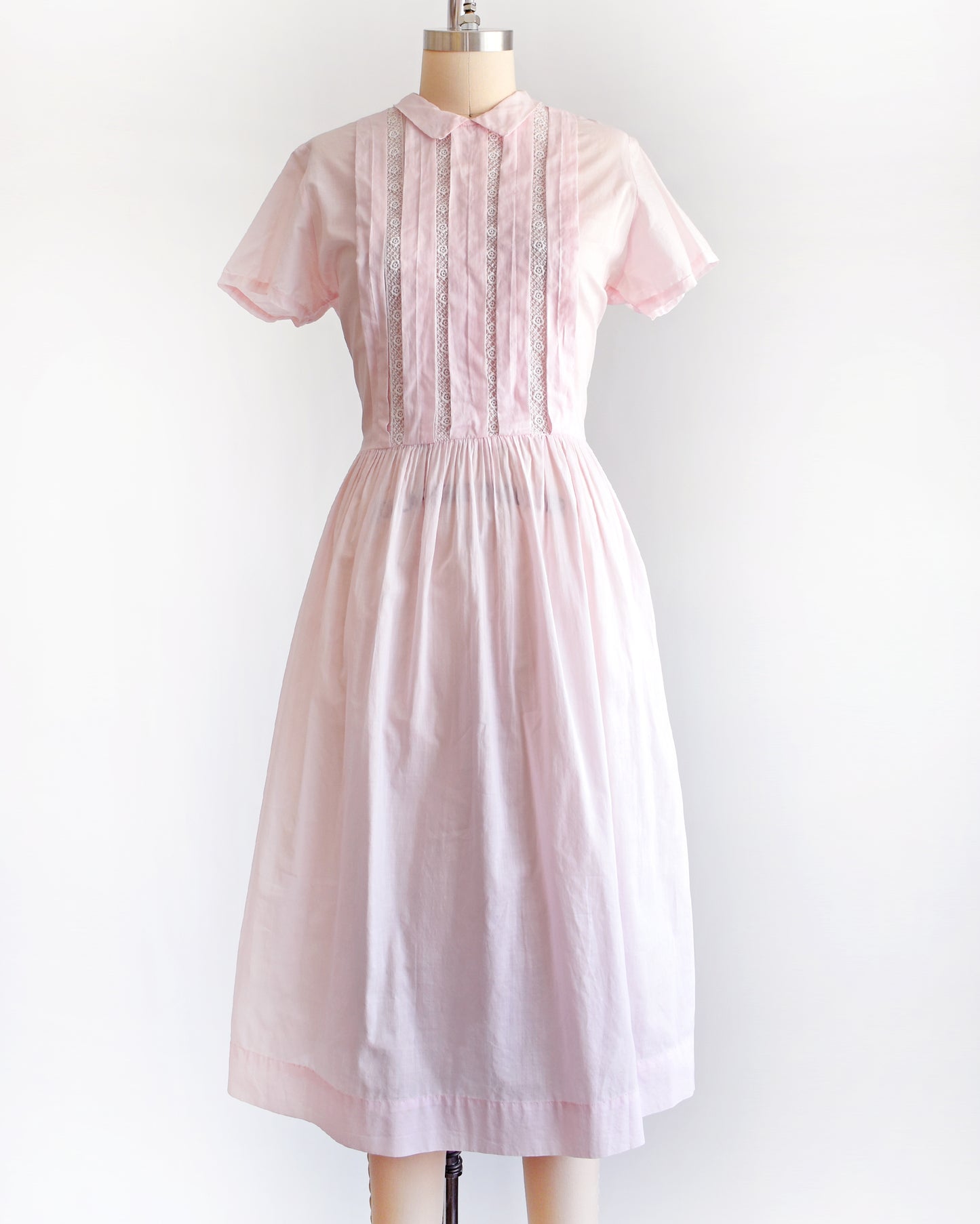 a vintage 1950s pink dress on a mannequin against a white background