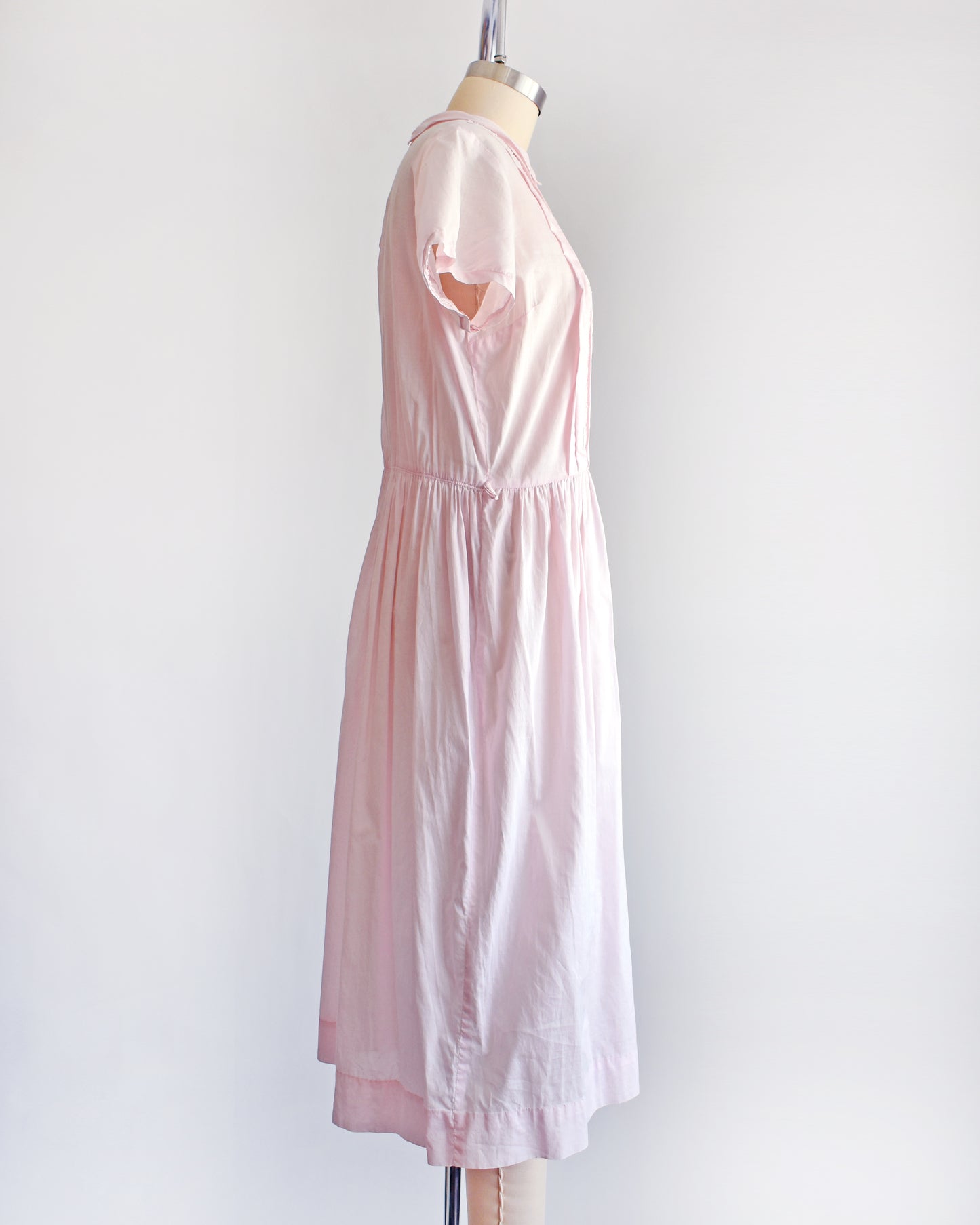 side view of a vintage 1950s pink dress on a mannequin against a white background