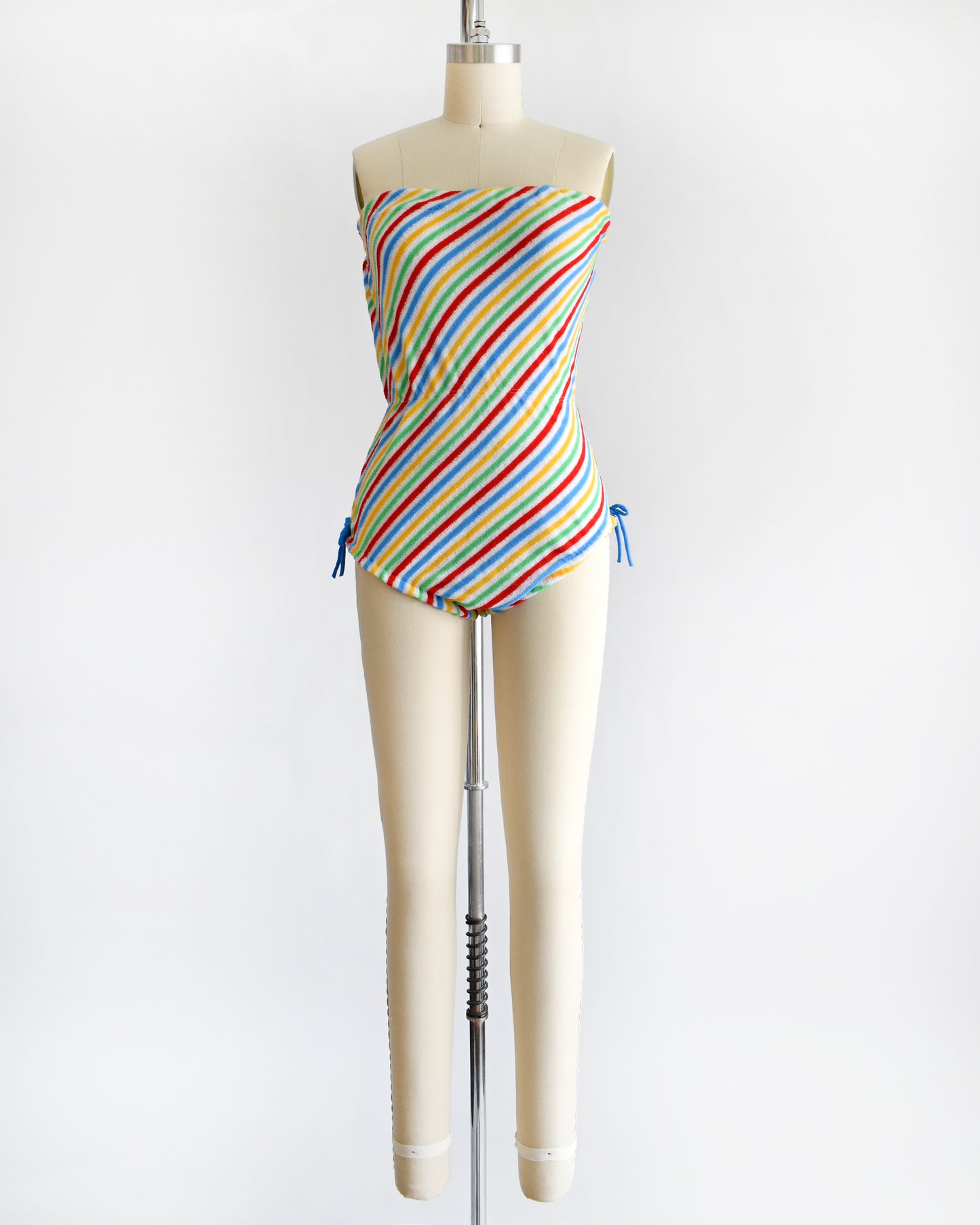 a vintage 1970s romper that is white with red, green, yellow, and blue diagonal stripes and blue bows on the hips