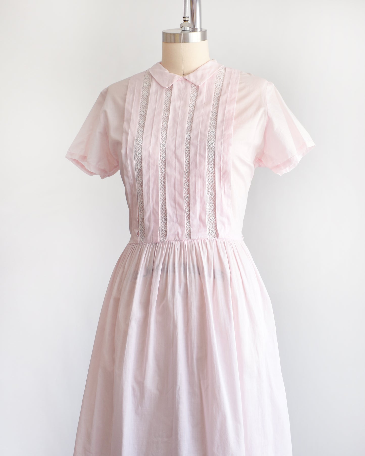 side front view of a vintage 1950s pink dress on a mannequin against a white background
