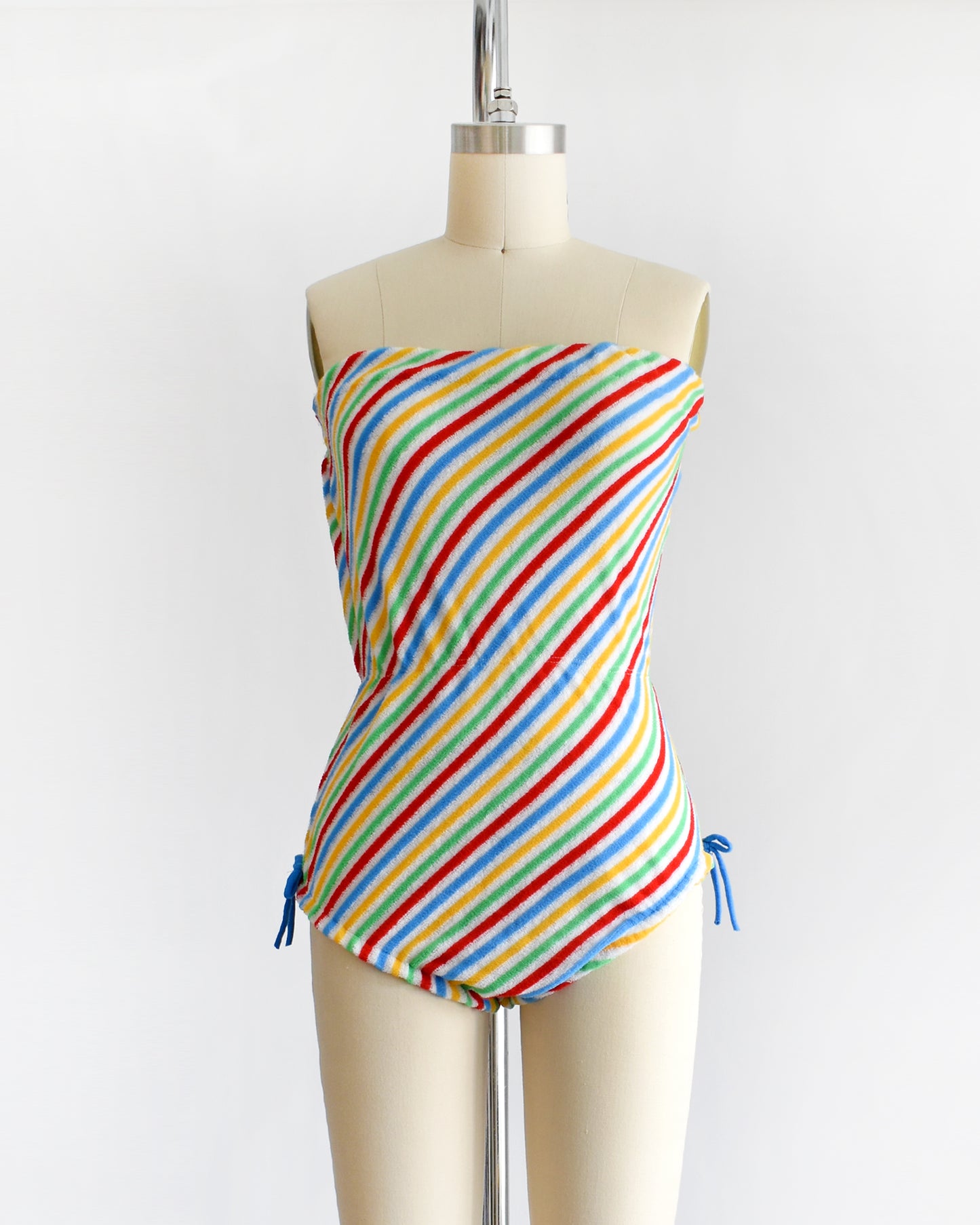 a vintage 1970s romper that is white with red, green, yellow, and blue diagonal stripes and blue bows on the hips