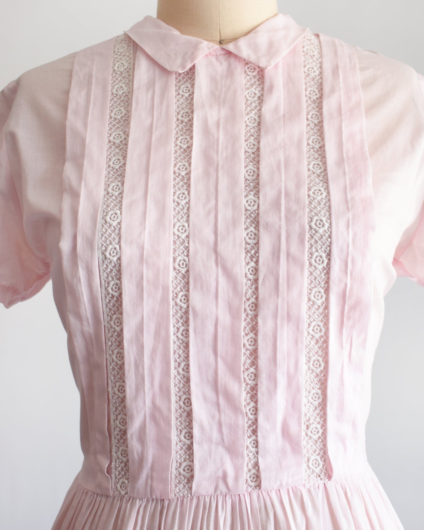 close up of a vintage 1950s pink dress that shows the white floral lace detail on a mannequin against a white background
