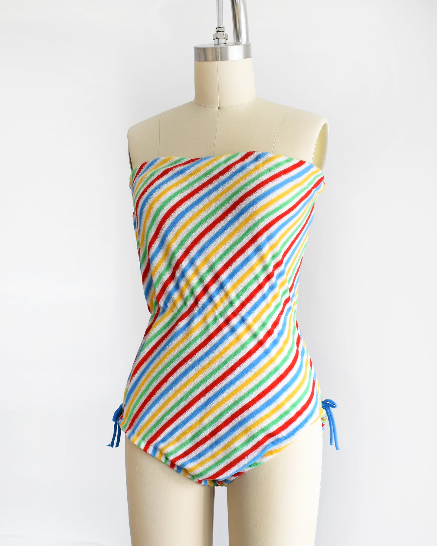 side front view of a vintage 1970s romper that is white with red, green, yellow, and blue diagonal stripes and blue bows on the hips