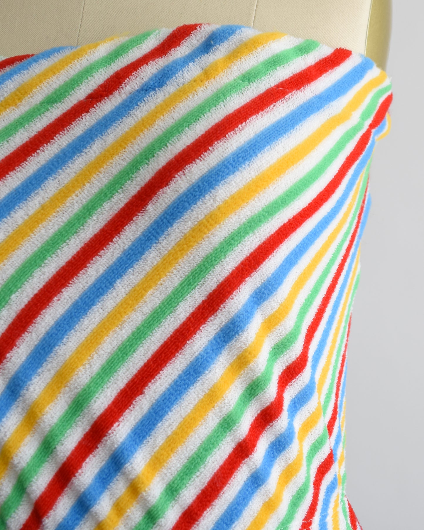 close up of a vintage 1970s romper that is white with red, green, yellow, and blue diagonal stripes