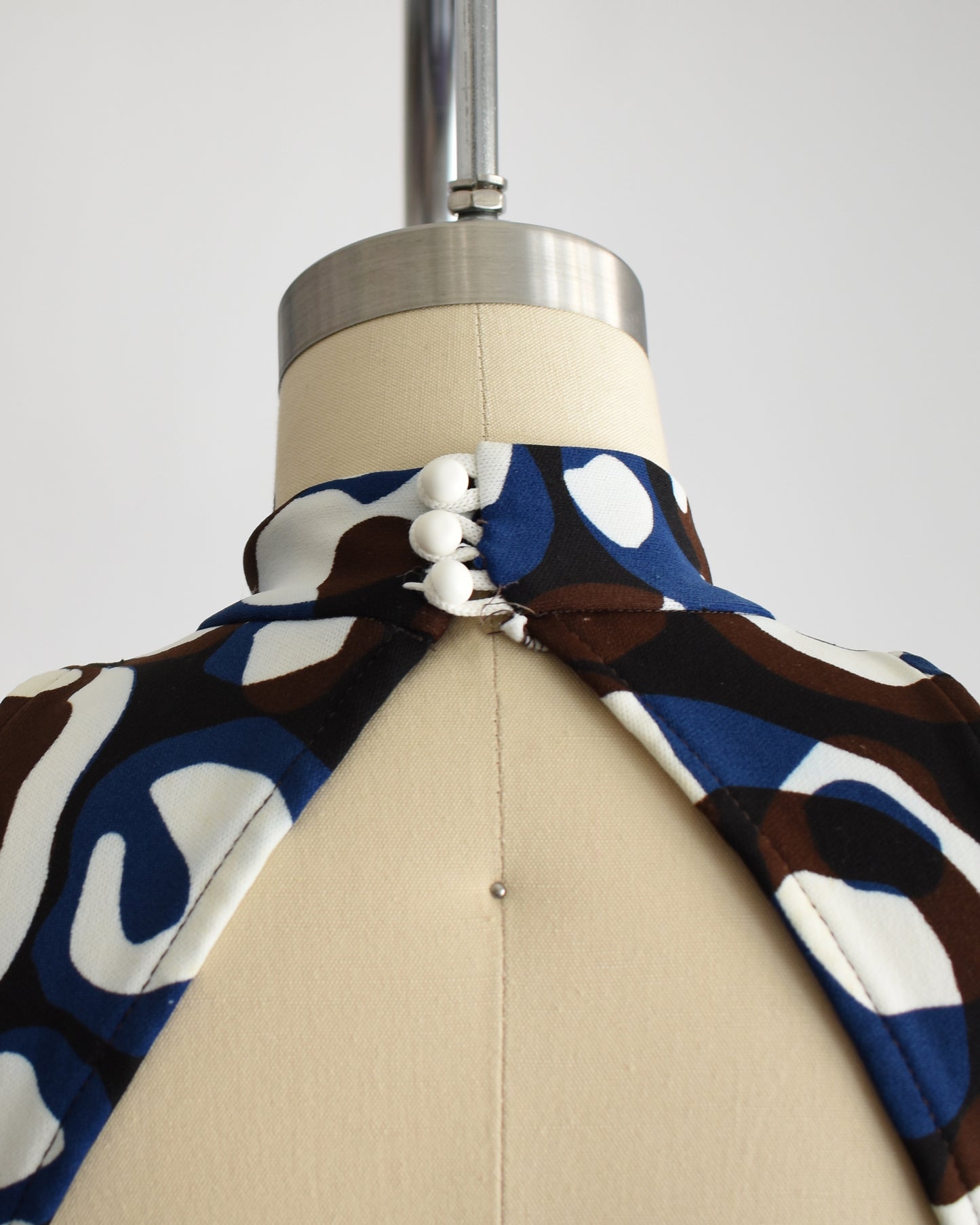 close up of the buttons on the back of the neck on a vintage 1960s psychedelic swimsuit on a mannequin against a white background