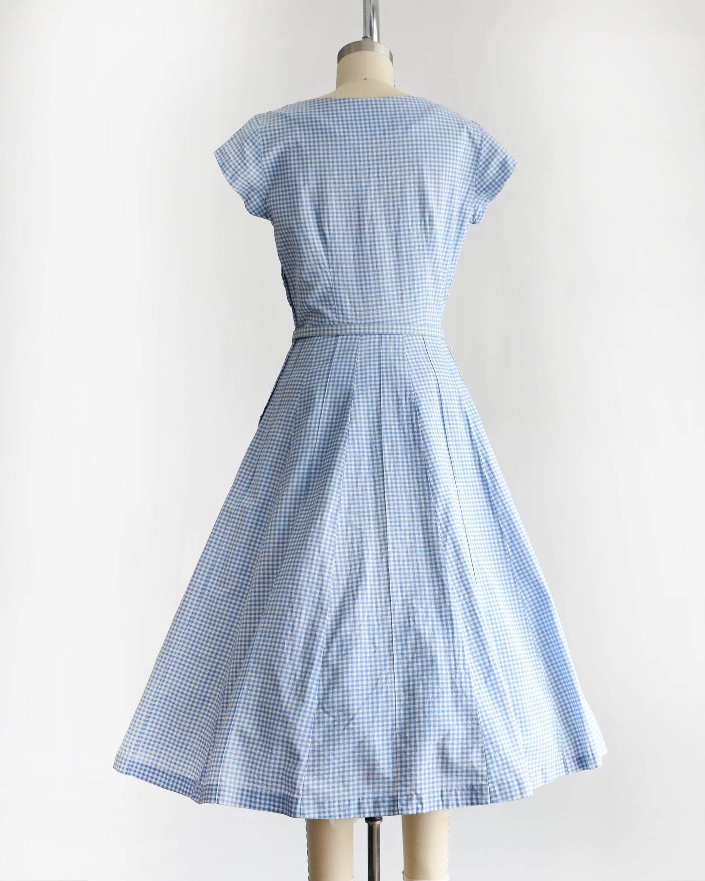 back view of a vintage 1950s blue and white gingham dress on a mannequin against a white background