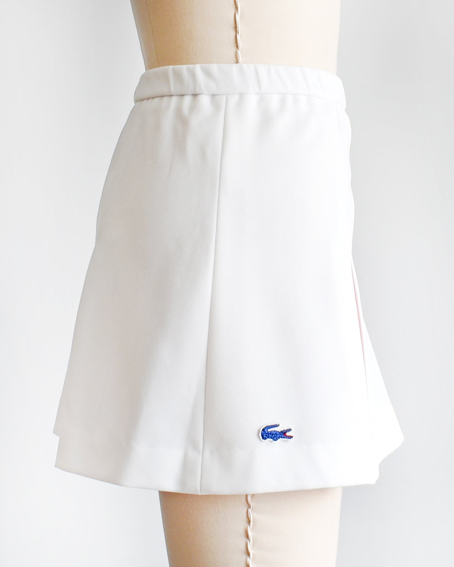 side view of a vintage 1970s Lacoste Haymaker skirt that has a blue Lacoste crocodile on the side on a mannequin against a white background