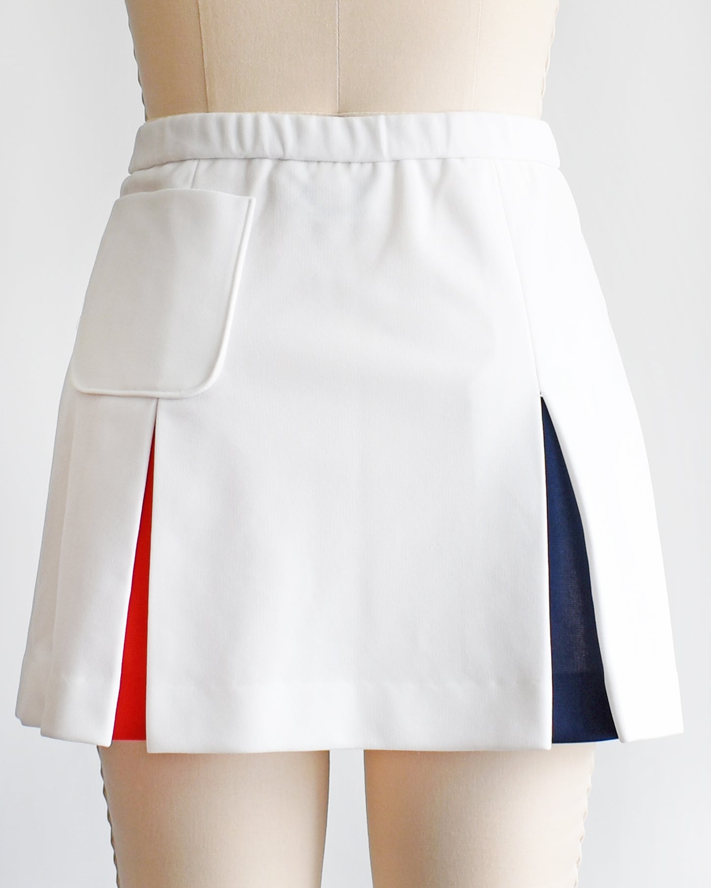 back view of a vintage 1970s Lacoste Haymaker skirt with red and blue accented pleats and a back pocket on a mannequin against a white background