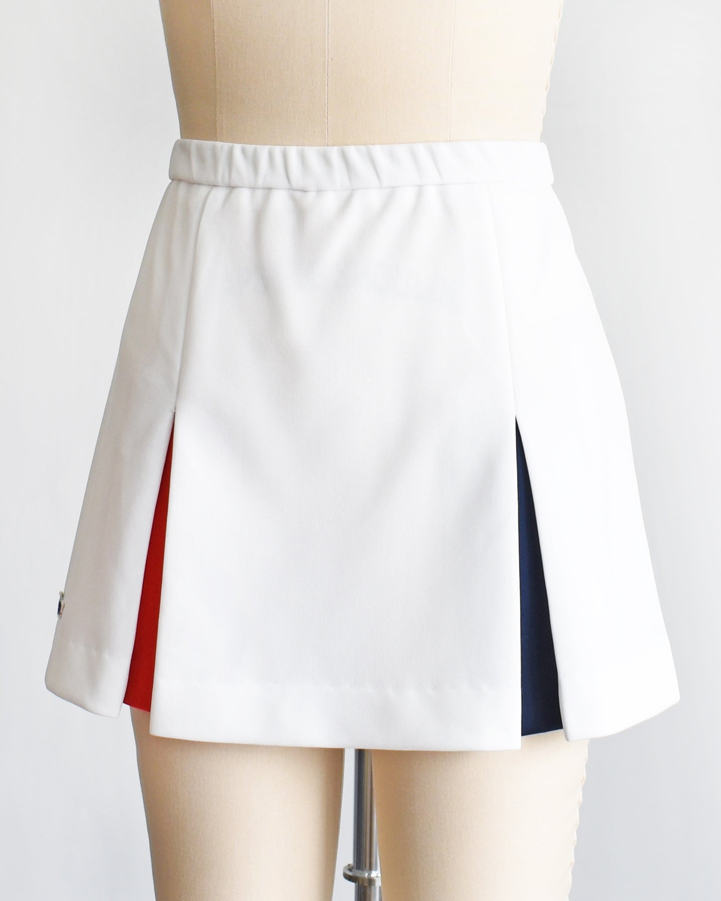 side front view of a vintage 1970s Lacoste Haymaker skirt with red and blue accented pleats on a mannequin against a white background