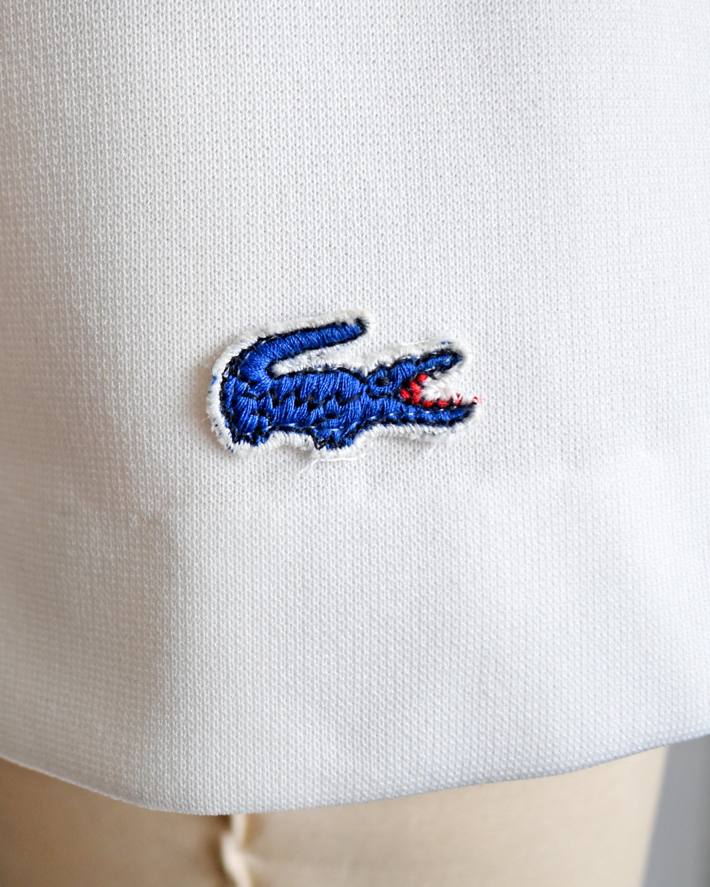 Close-up of a blue embroidered Lacoste crocodile logo on the side of the white skirt