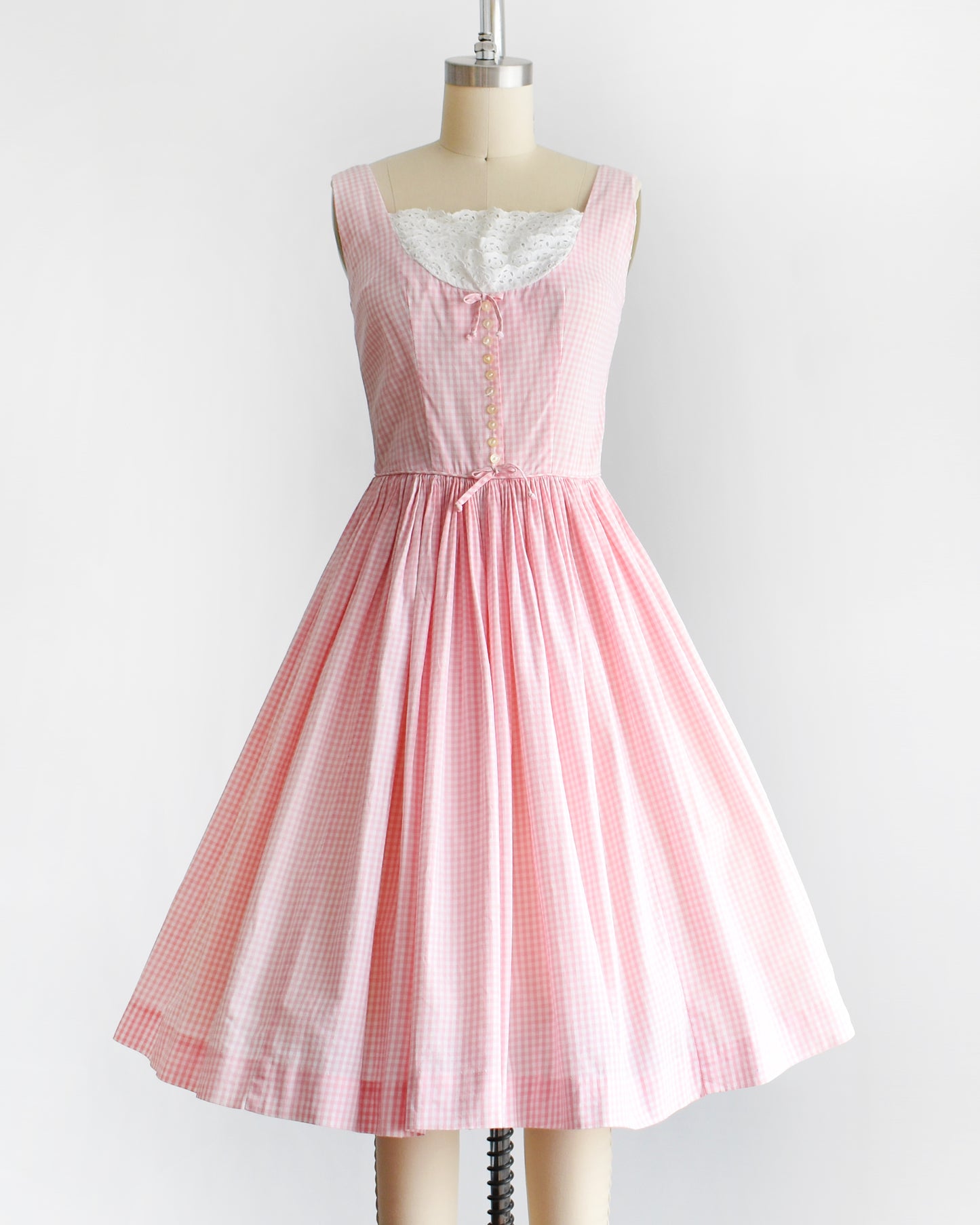 a vintage 1950s pink and white gingham dress on a mannequin against a white background