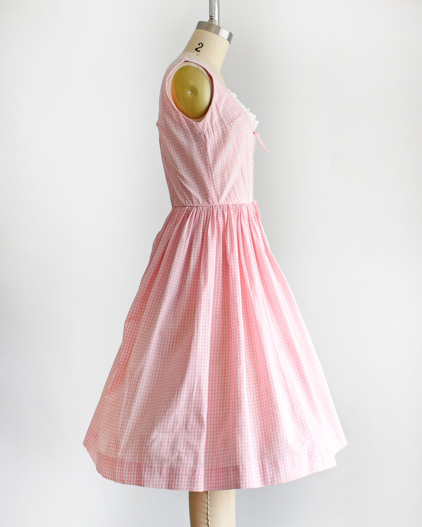side view of a vintage 1950s pink and white gingham dress on a mannequin against a white background