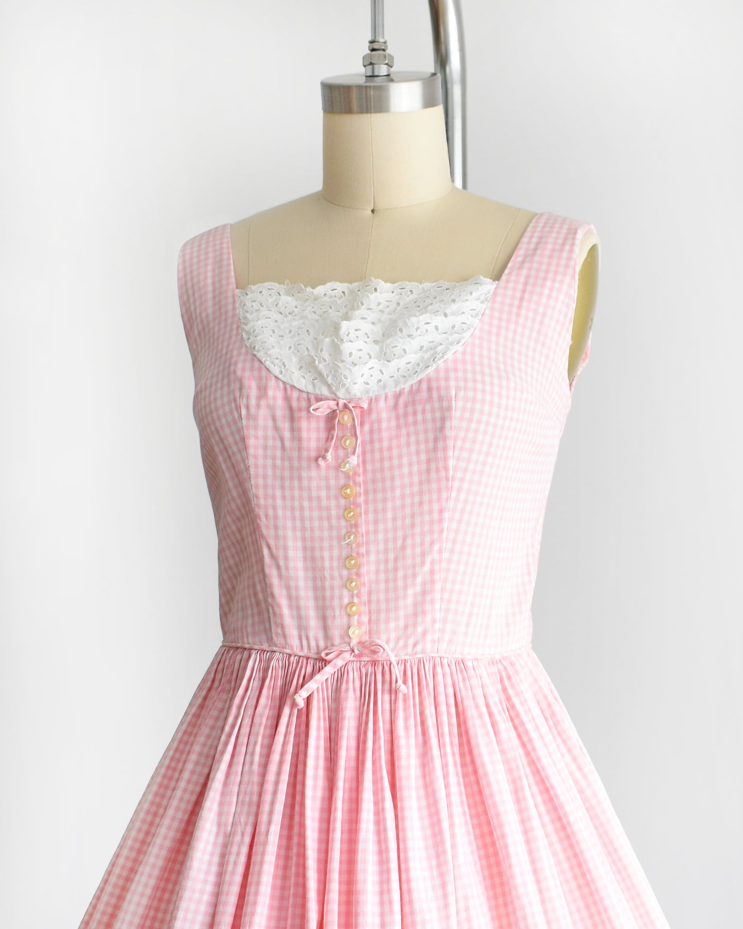 side front view of a vintage 1950s pink and white gingham dress on a mannequin against a white background