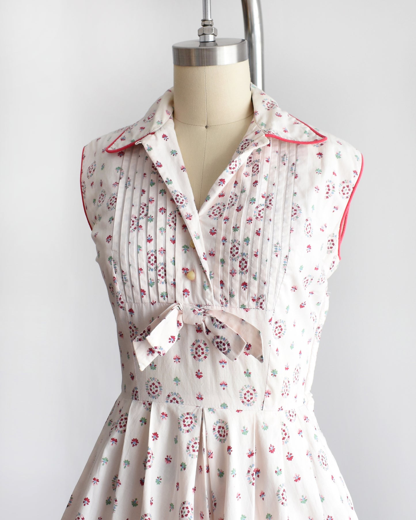 side front view of a vintage 1950s floral dress on a mannequin against a white background. the top button is unbuttoned